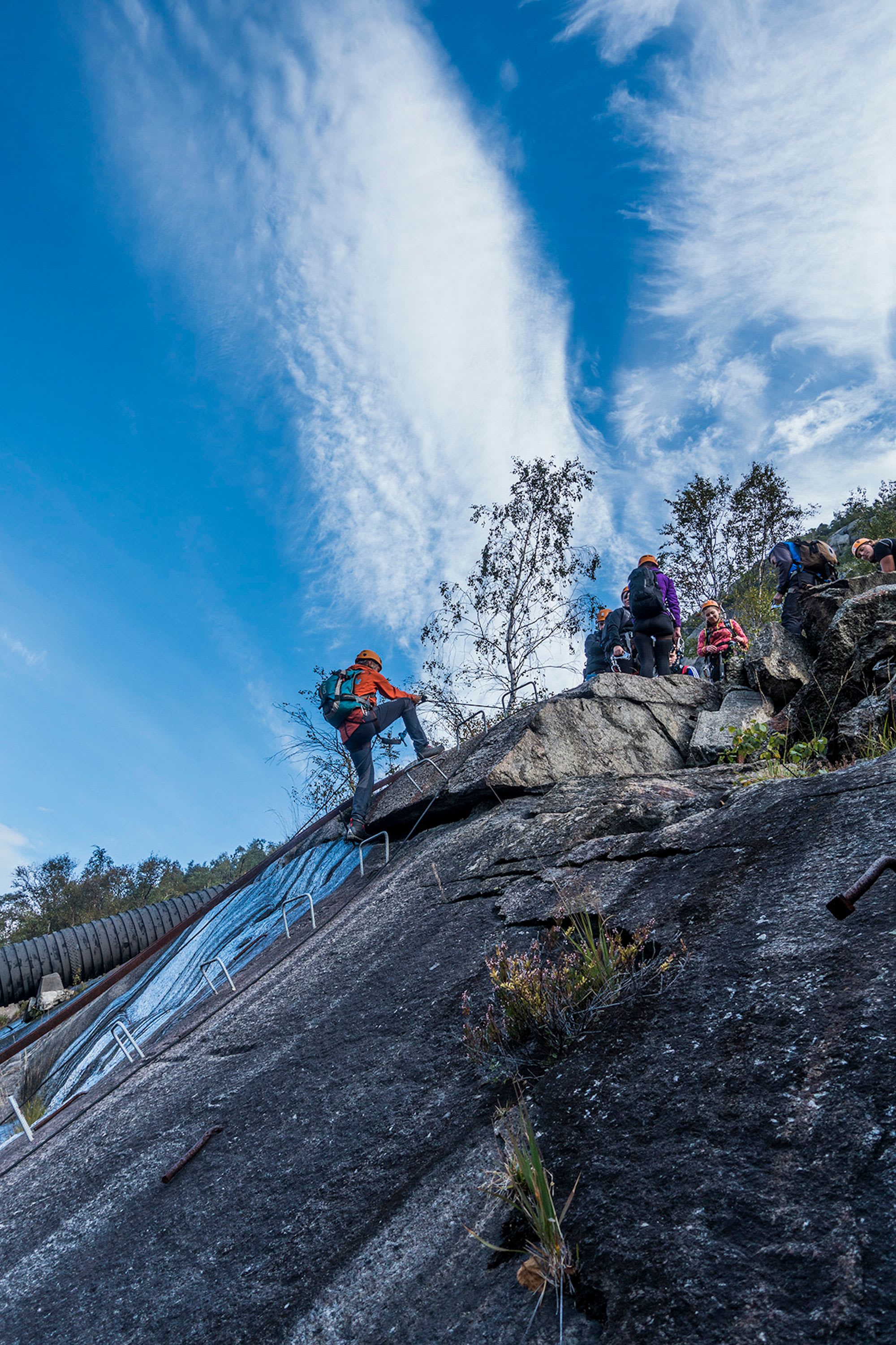 Klatrer klatrer via ferrata, gruppe venter over på solrik dag.