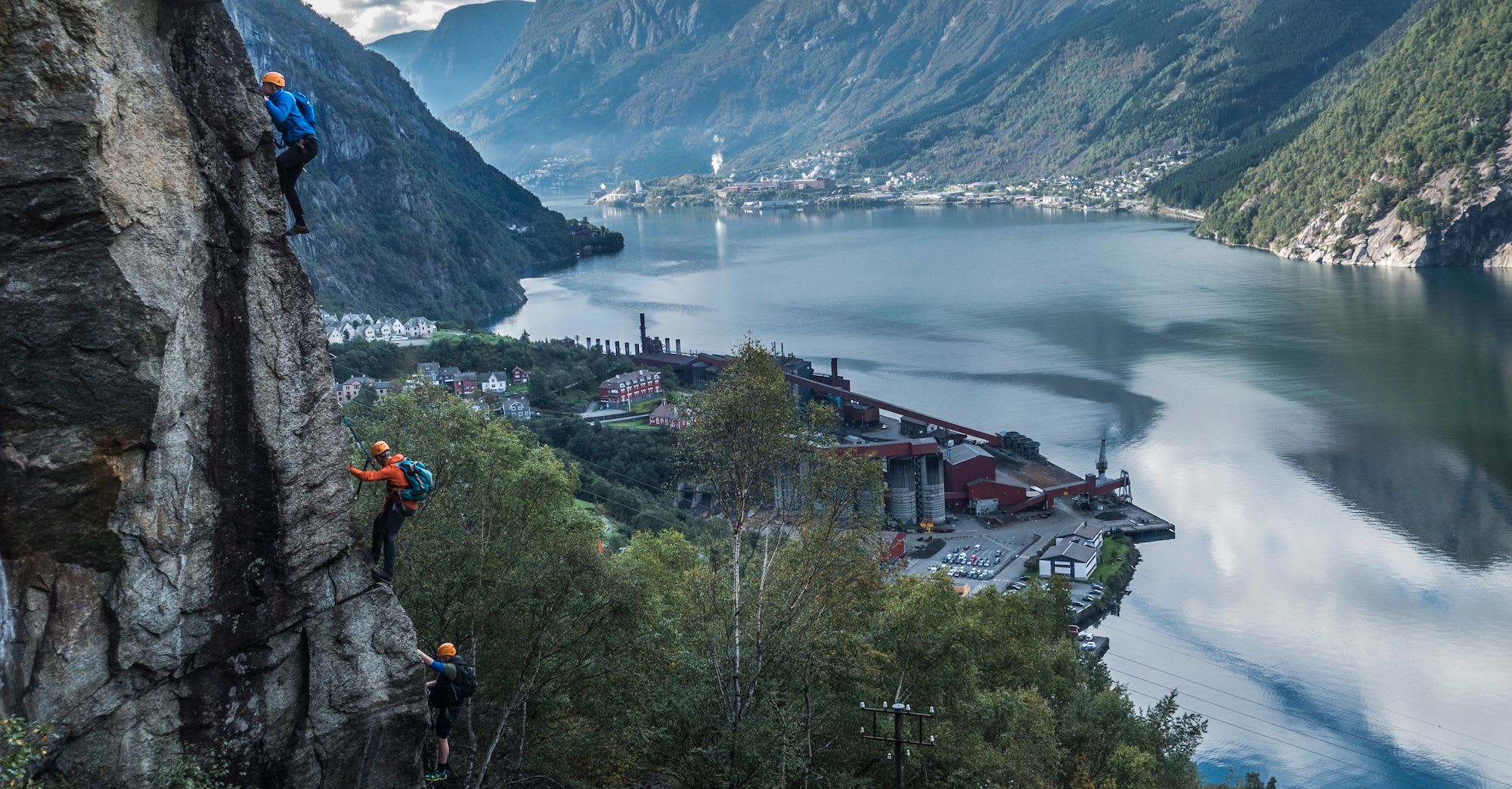Klatrere klatrer over fjord med fabrikk og fjell.