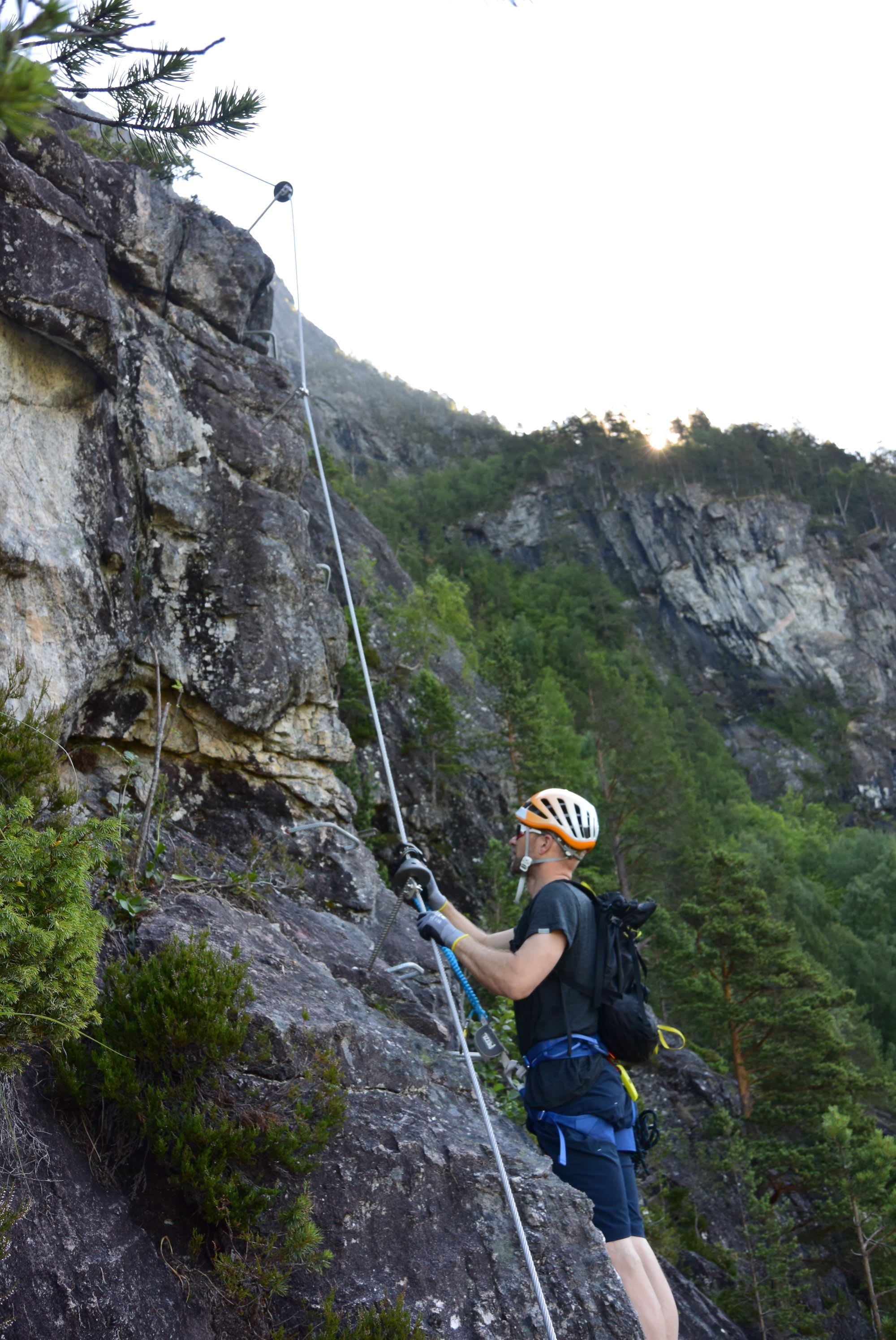 Klatrer klatrer bratt fjell i solnedgang, sikret med tau og utstyr.