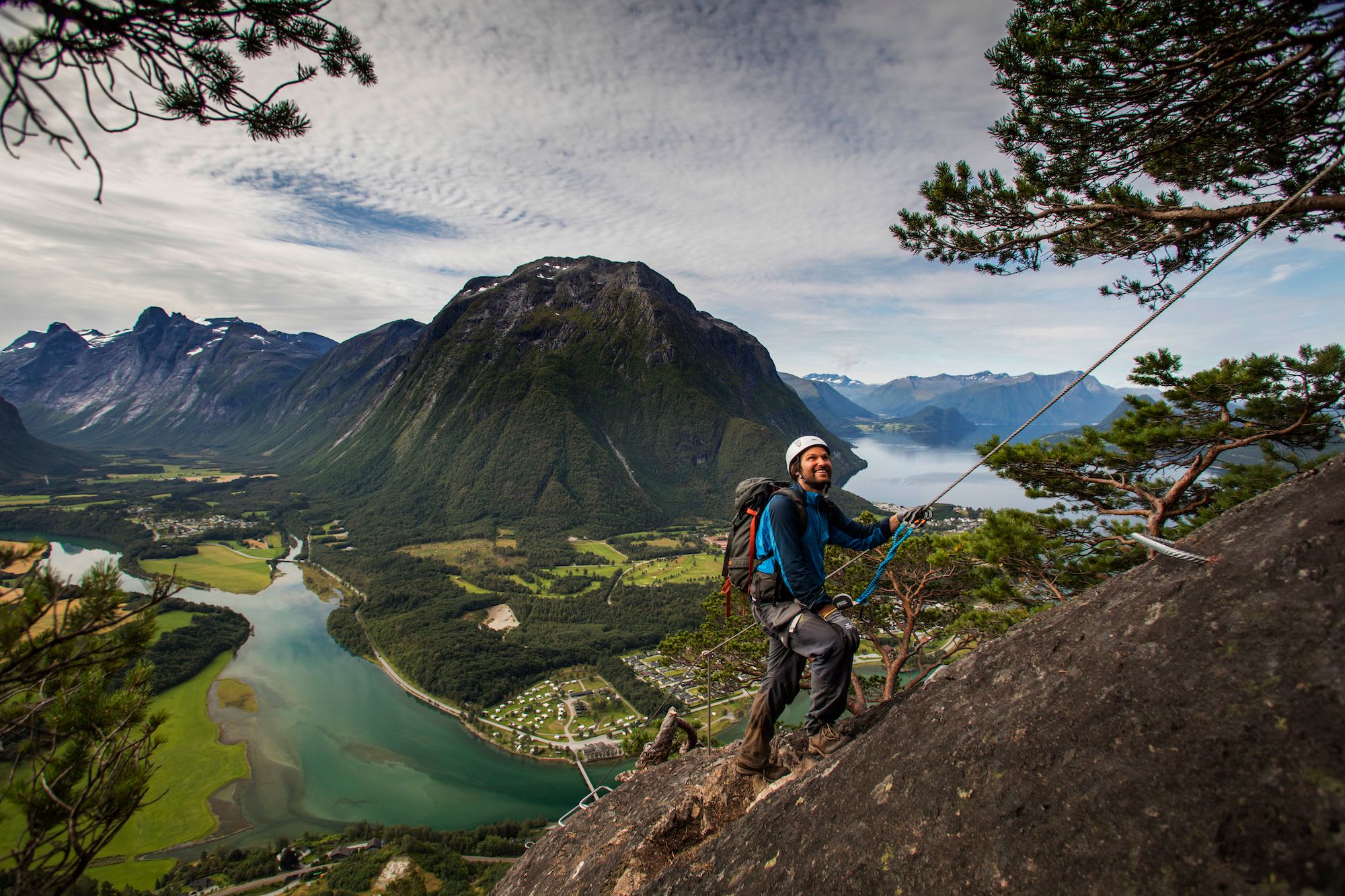 Klatrer smiler på klippe med dal og fjord under.