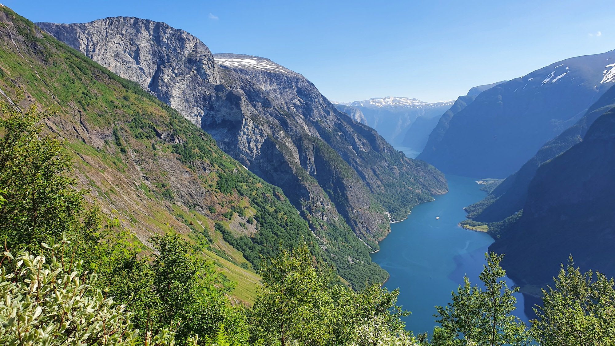 Dyp blå fjord mellom snødekte fjell under blå himmel.