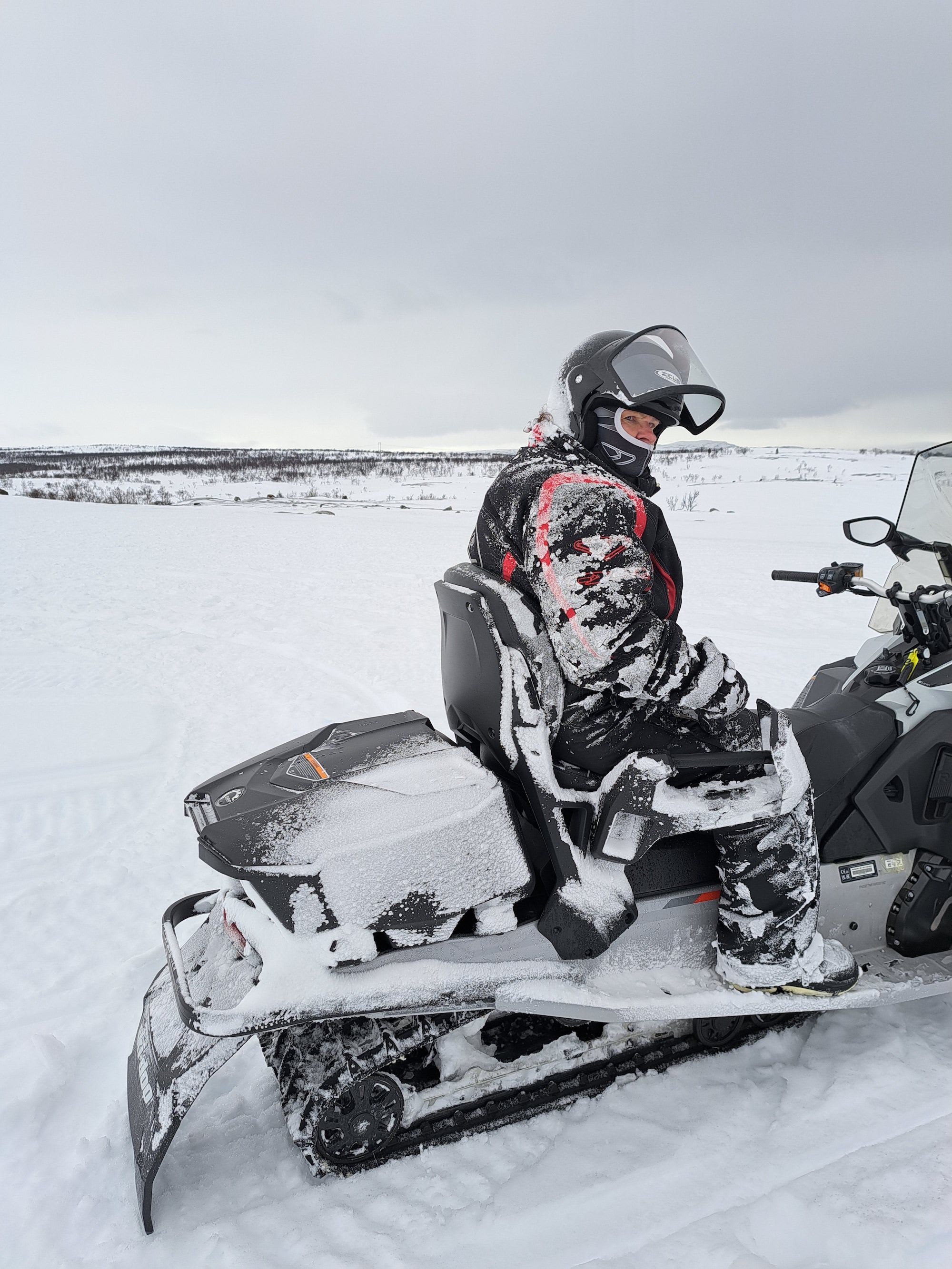 A snowmobiler, covered in fresh snow, sits in a vast Arctic landscape.