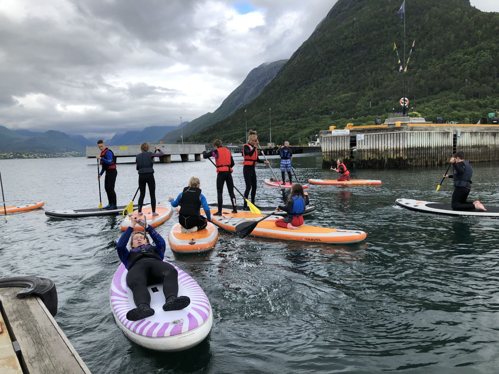 A group of people paddleboarding near a harbor, surrounded by lush green mountains.