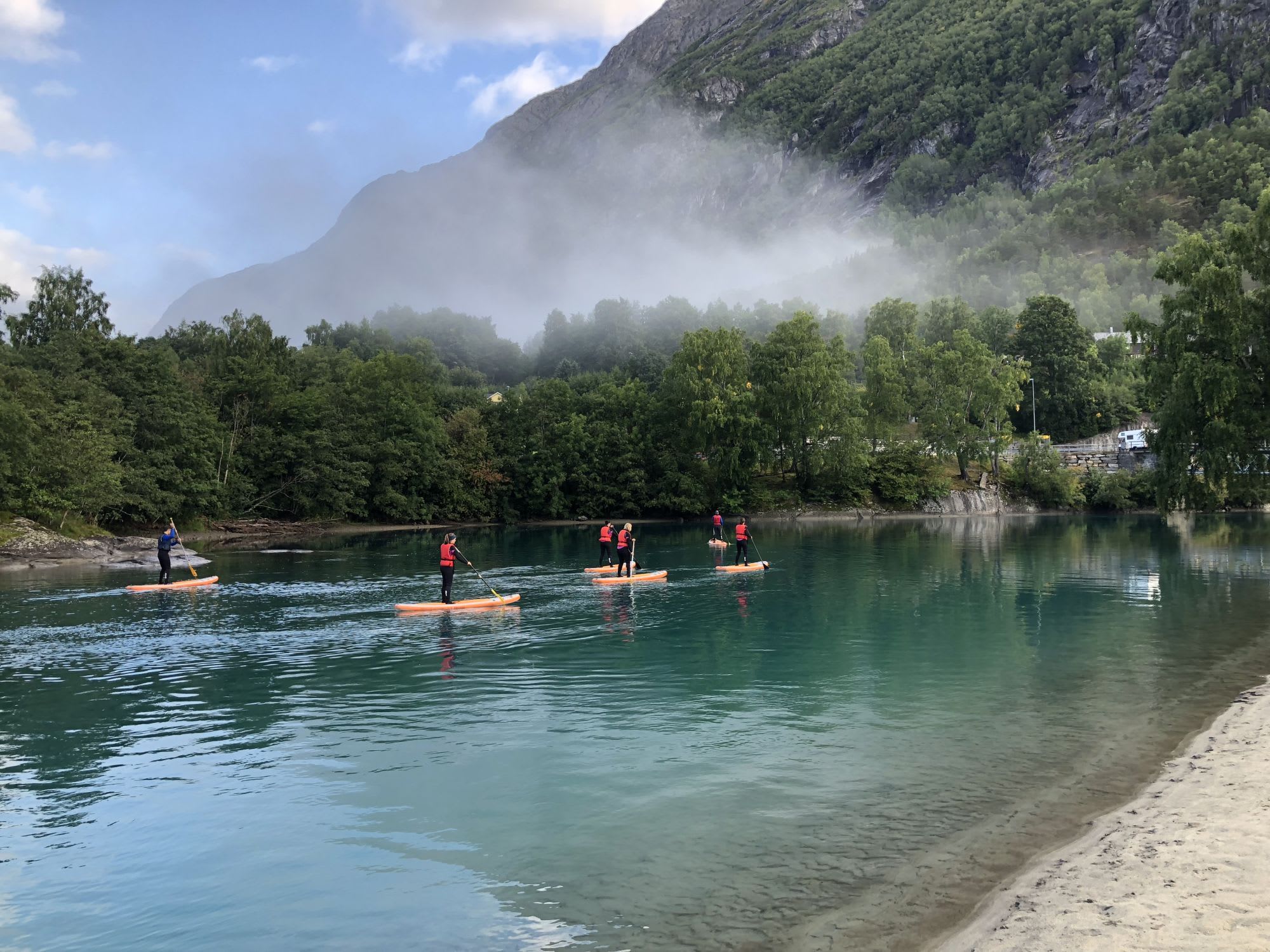 Six people paddleboarding on a crystal-clear river near the bay, with the riverbed visible.