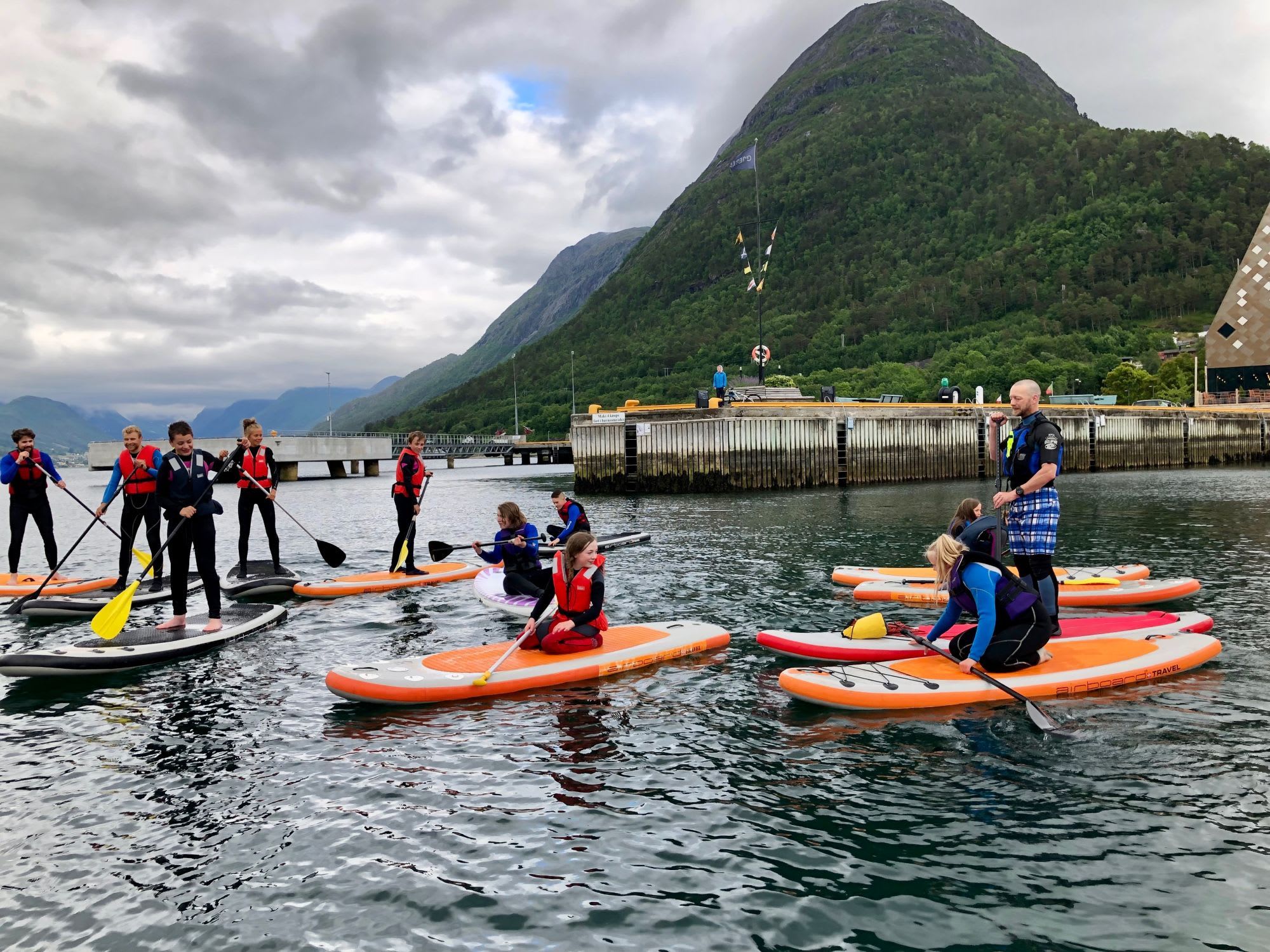 People paddleboarding near a wooden pier, some standing, others kneeling.