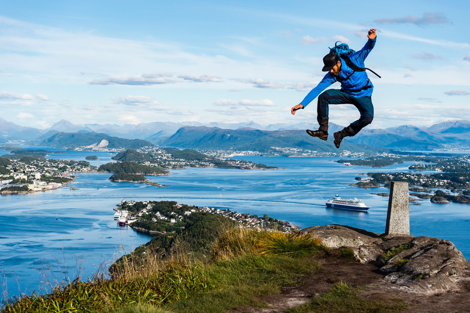 En eventyrer hopper fra en stein på toppen av et fjell, med en fantastisk utsikt over kysten og byen nedenfor.