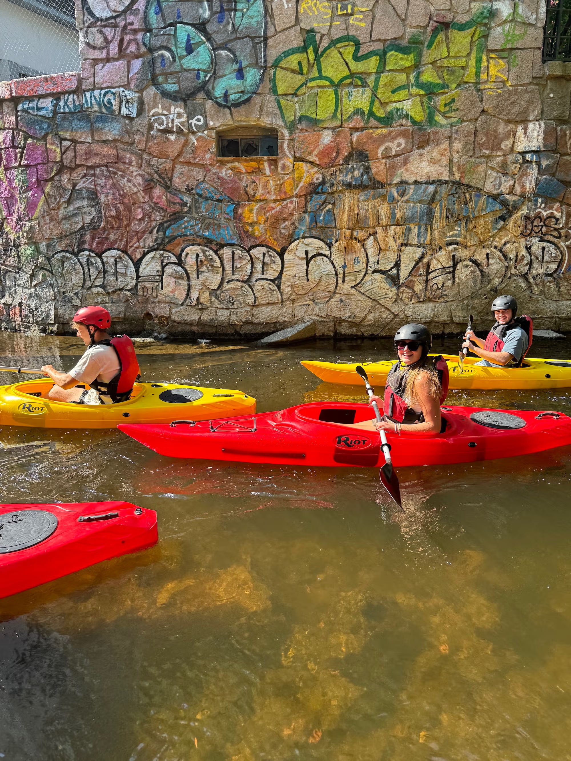 Kajakpadlere passerer fargerik graffiti-vegg ved elva