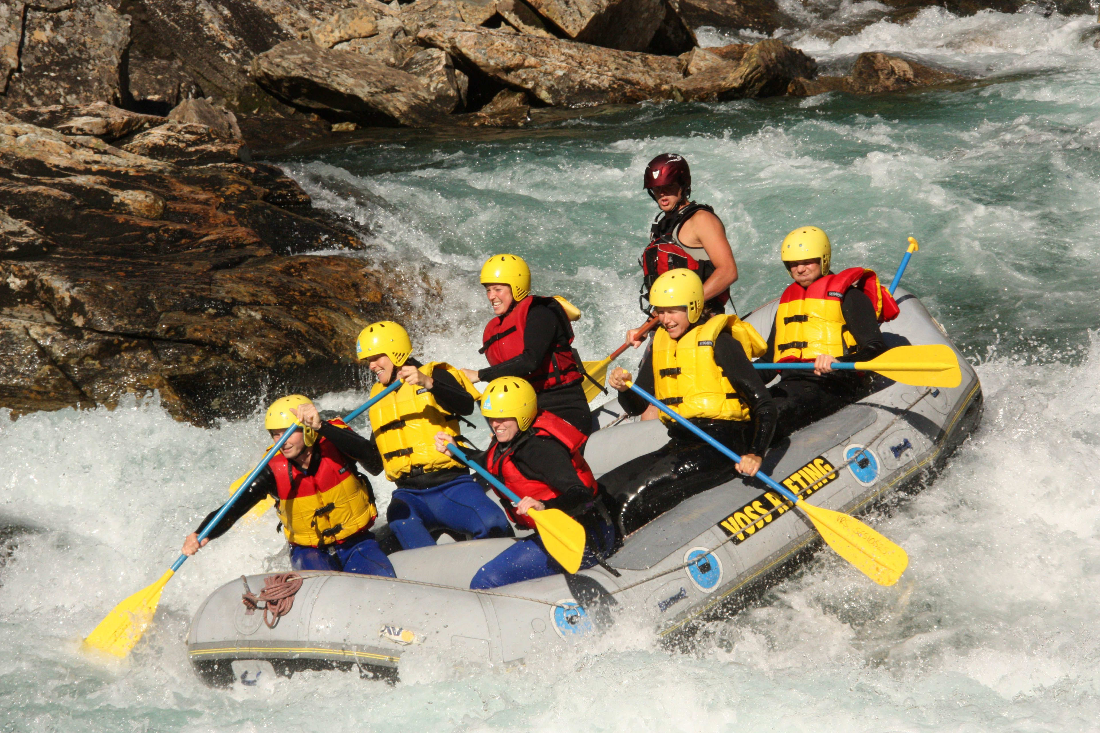 Seven individuals paddling in a raft through fast-moving water, with a guide managing the direction.