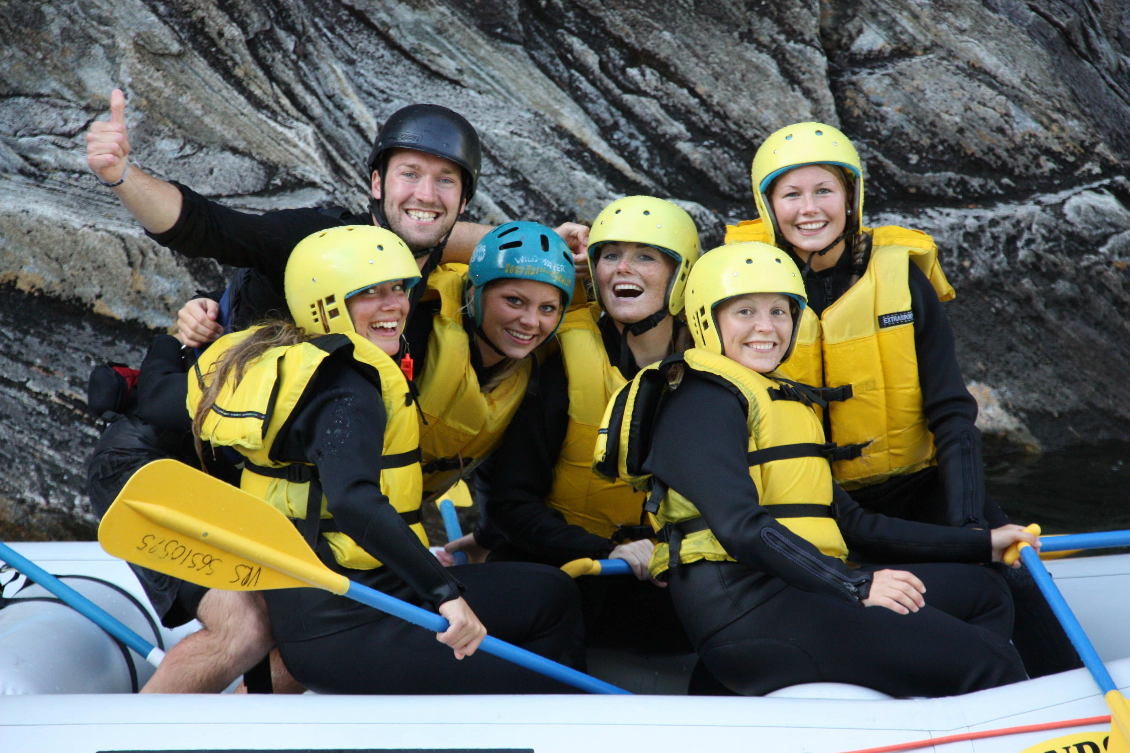 A group of six people smiling and enjoying rafting together in a raft.