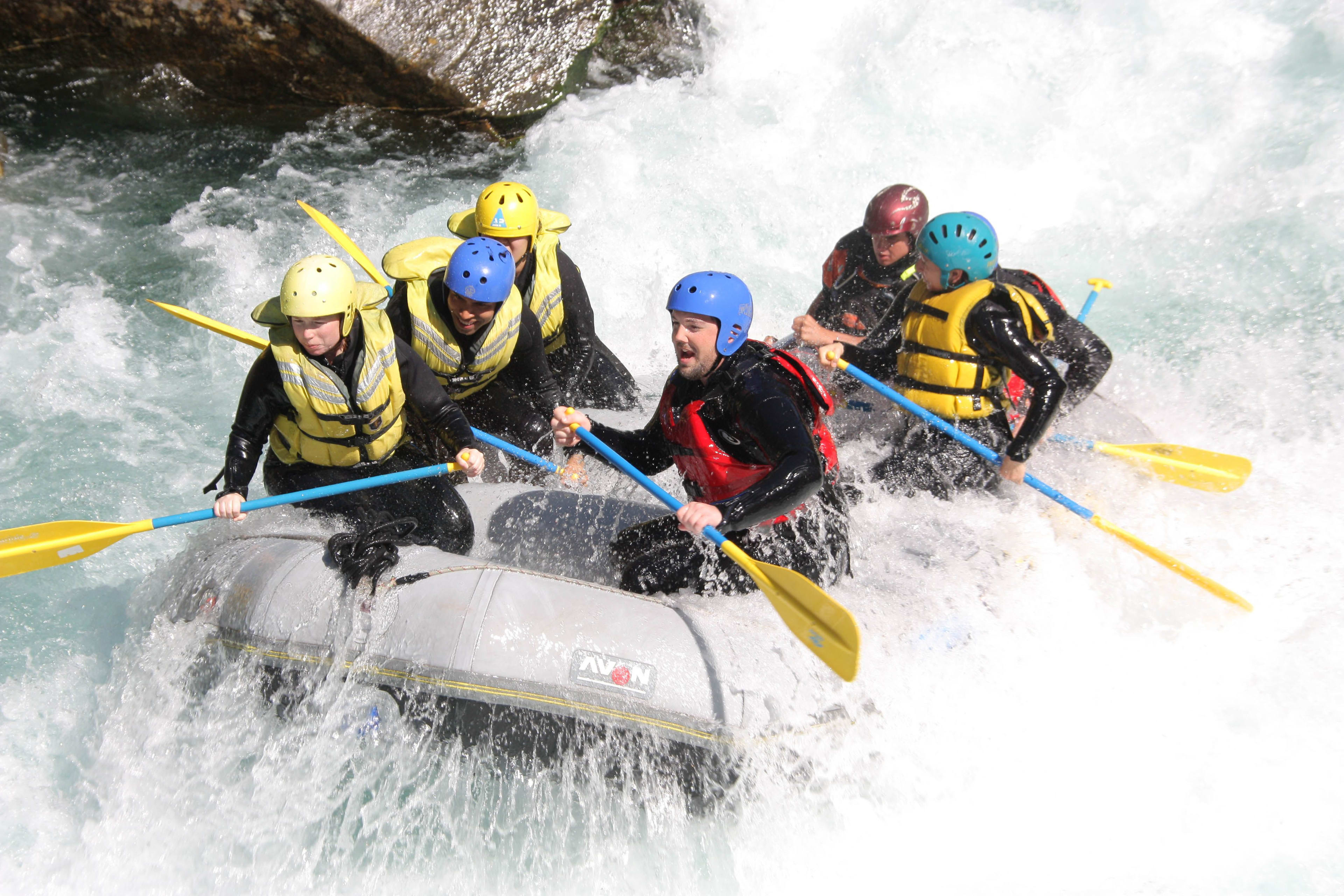 A group of six people actively rafting in turbulent water, paddling through strong waves.