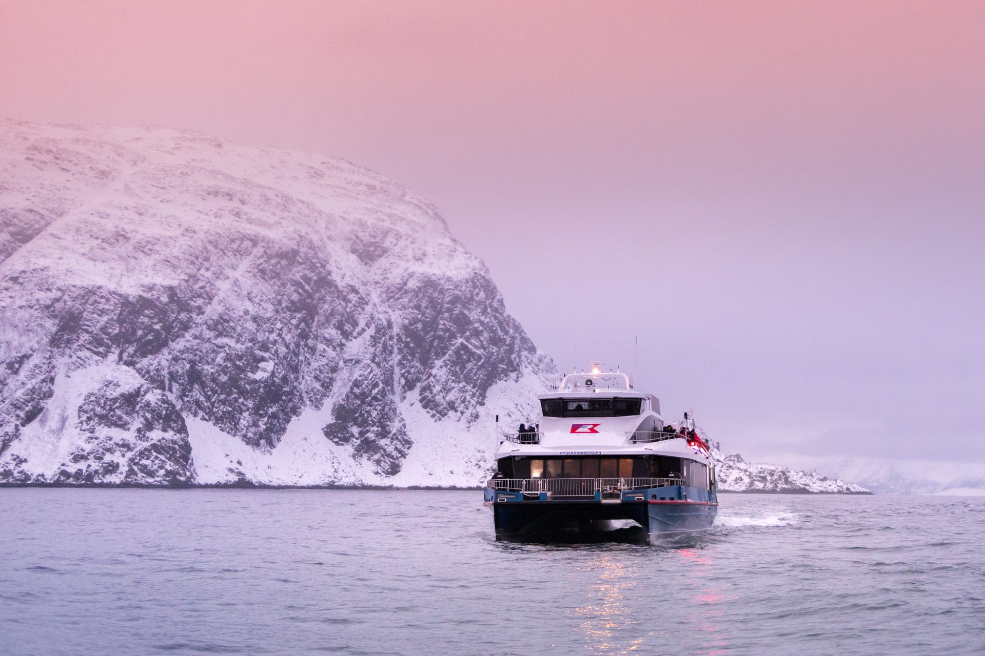 Walsafari-Boot fährt durch rosa arktische Dämmerung zu schneebedeckten Bergen nahe Tromsø Norwegen