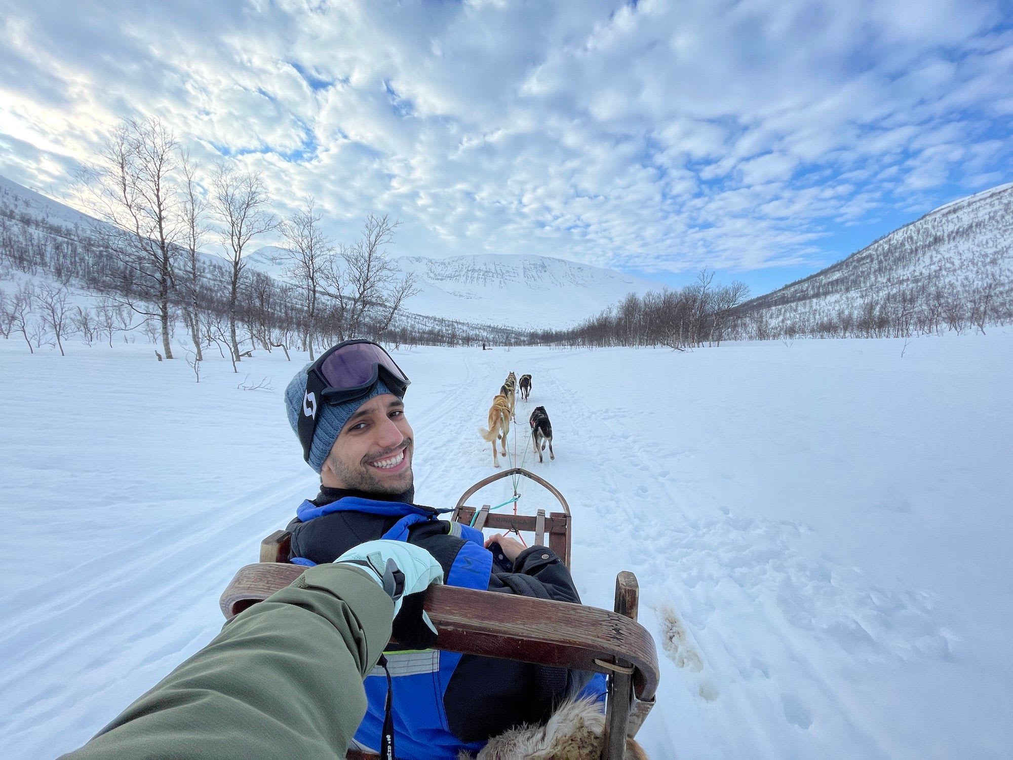 A person sitting in a dog sled, smiling joyfully as they enjoy the snowy landscape with dogs pulling the sled.