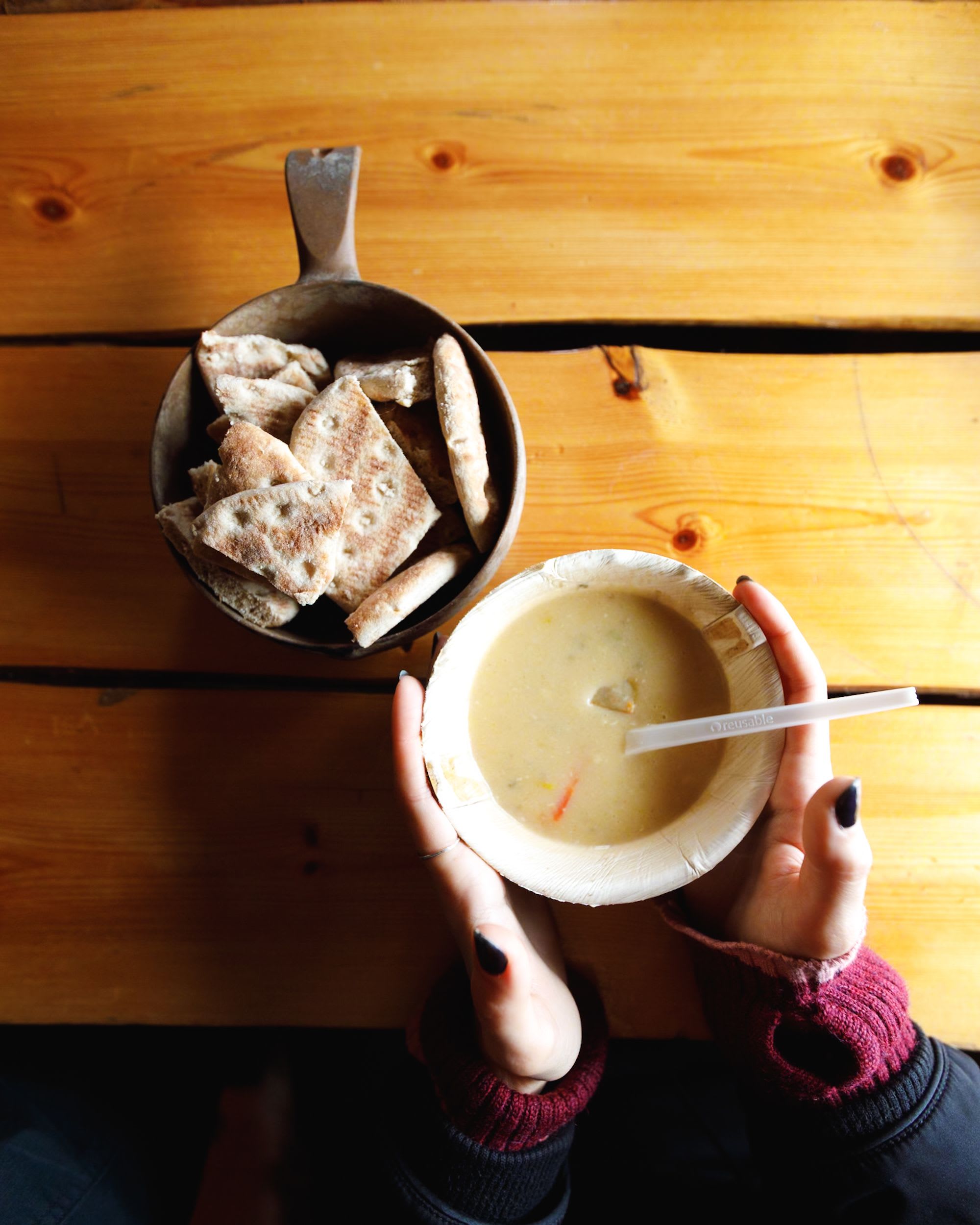 A person holds a bowl of creamy soup, with flatbread pieces beside it on a wooden table.