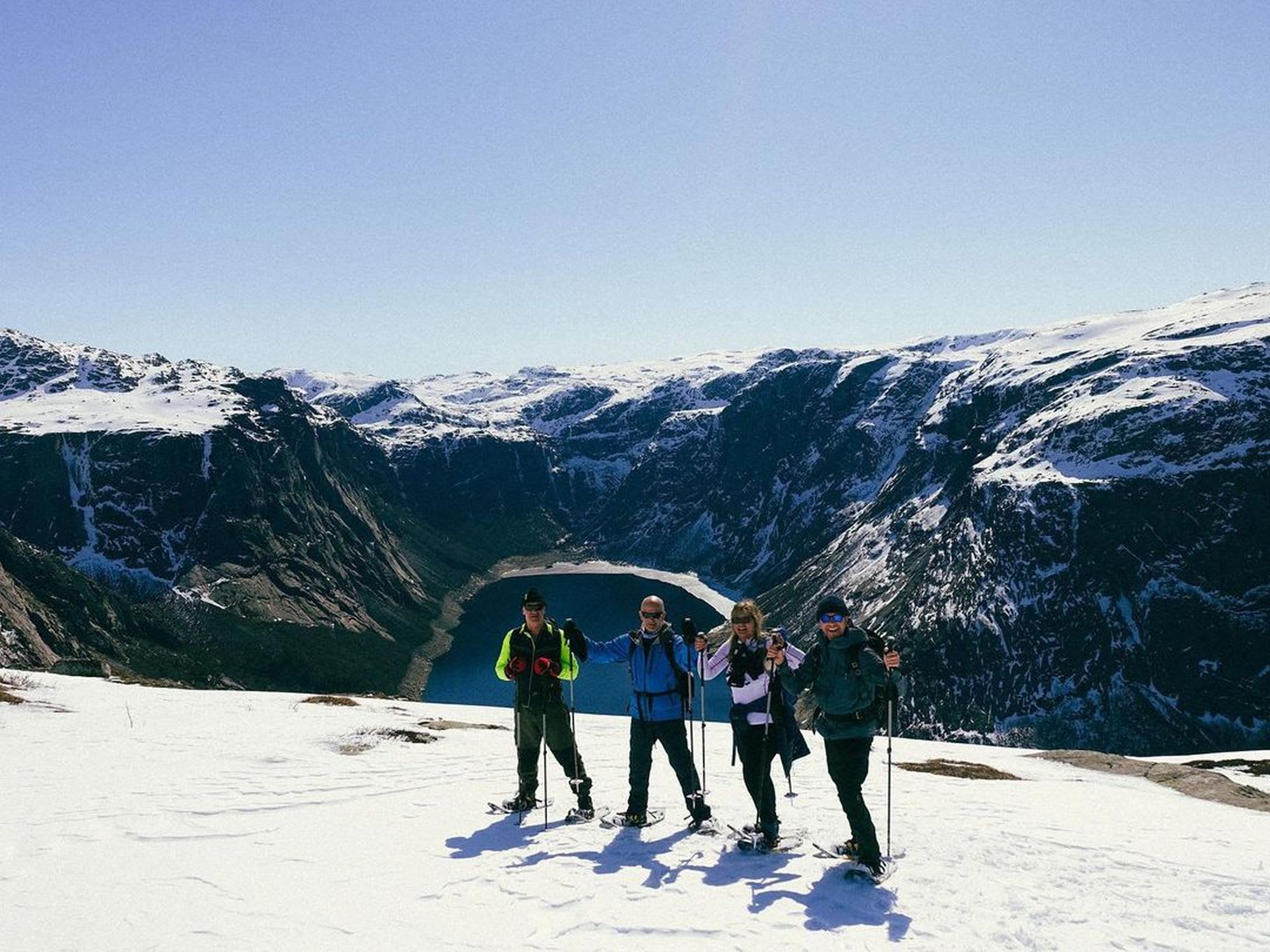 Fire personer står på en snødekt topp og poserer for et bilde med snesko, med en fjord og fjell i bakgrunnen.