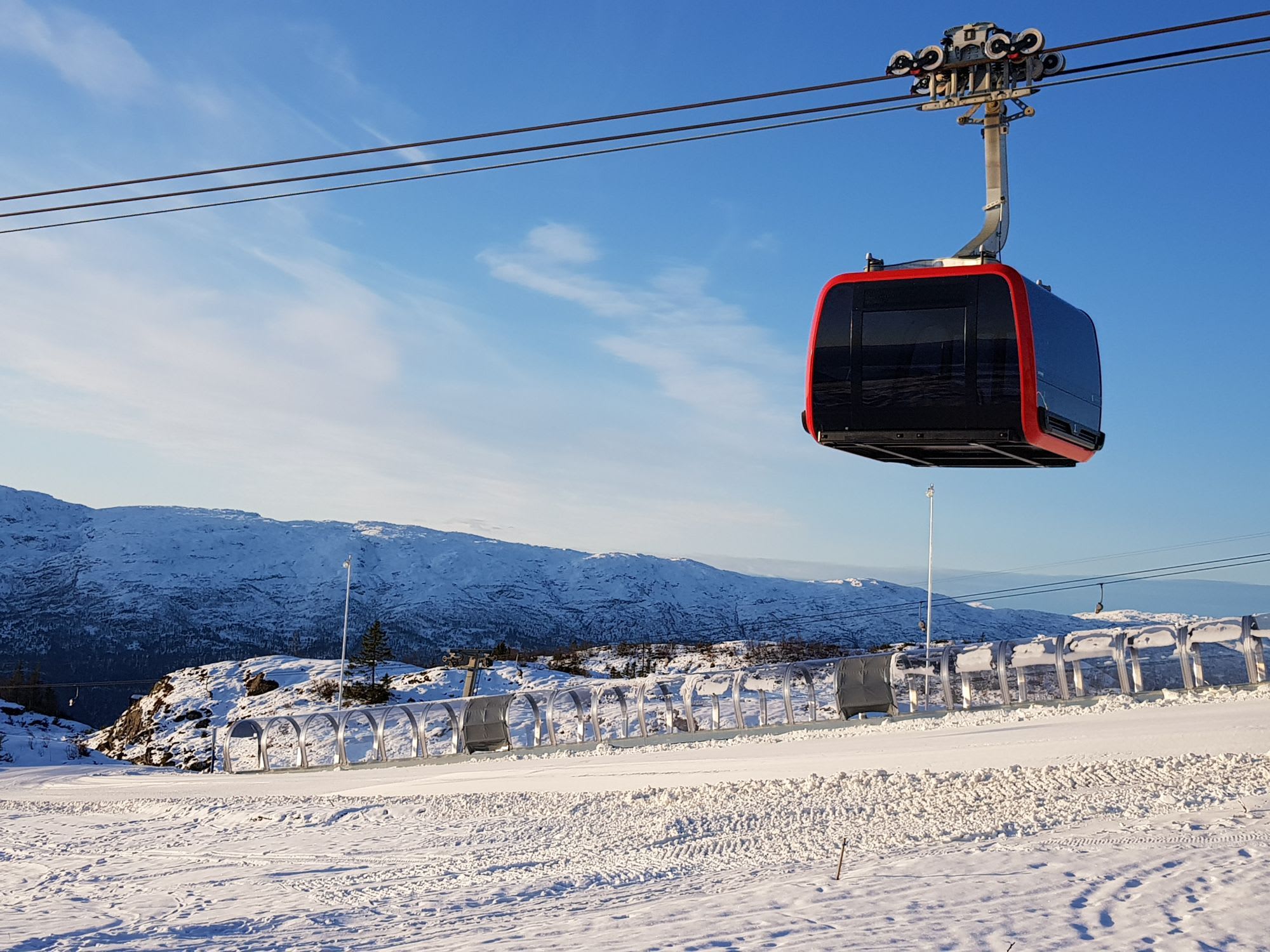 Red gondola over ski slope with conveyor lift and snowy peaks.
