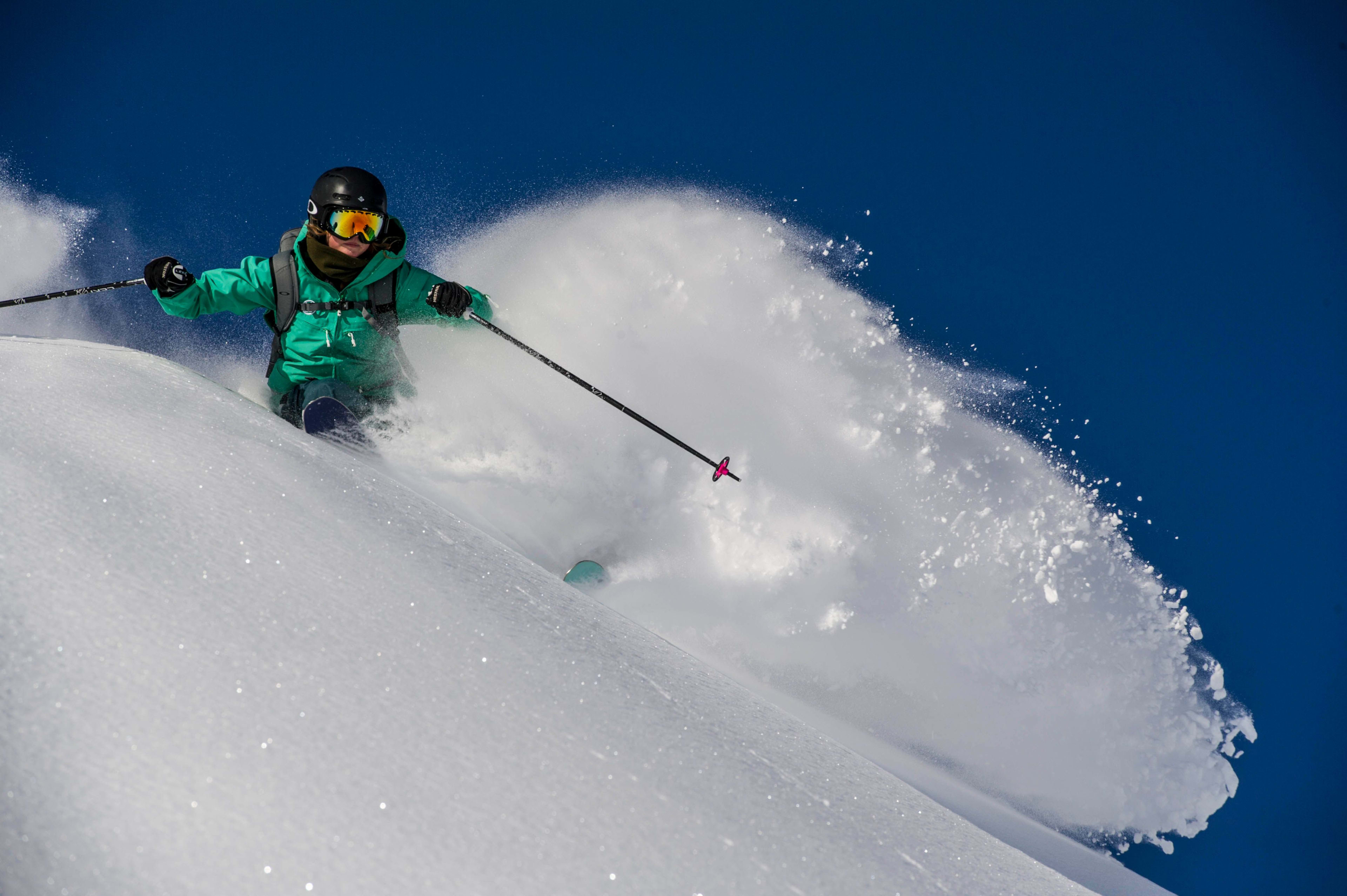 Ein Skifahrer in einer grünen Jacke fährt durch tiefen Schnee und hinterlässt eine Spur, mit einem strahlend blauen Himmel im Hintergrund.