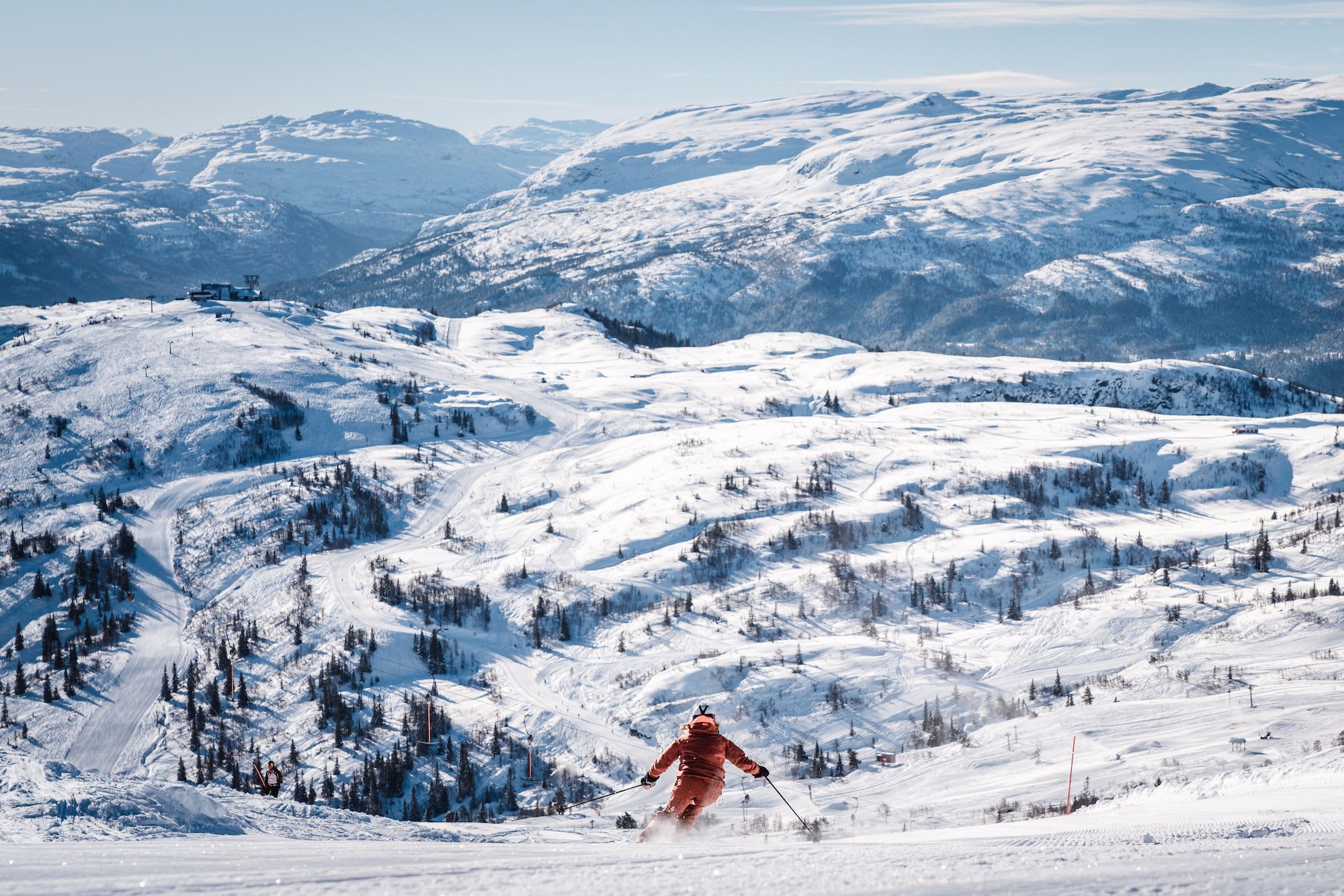A skier in bright orange gear descends a snow-covered slope, with smooth ski tracks visible.