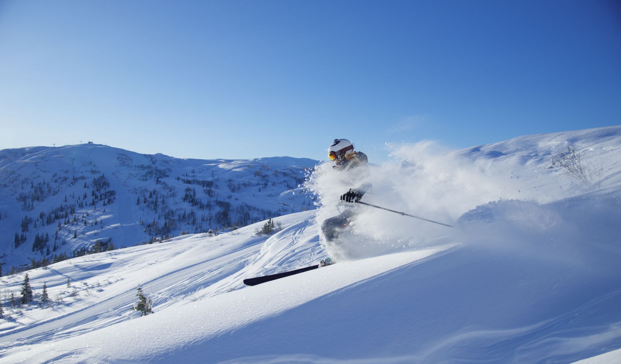 A skier carving through deep powder on a sunlit slope, kicking up a spray of fresh snow.
