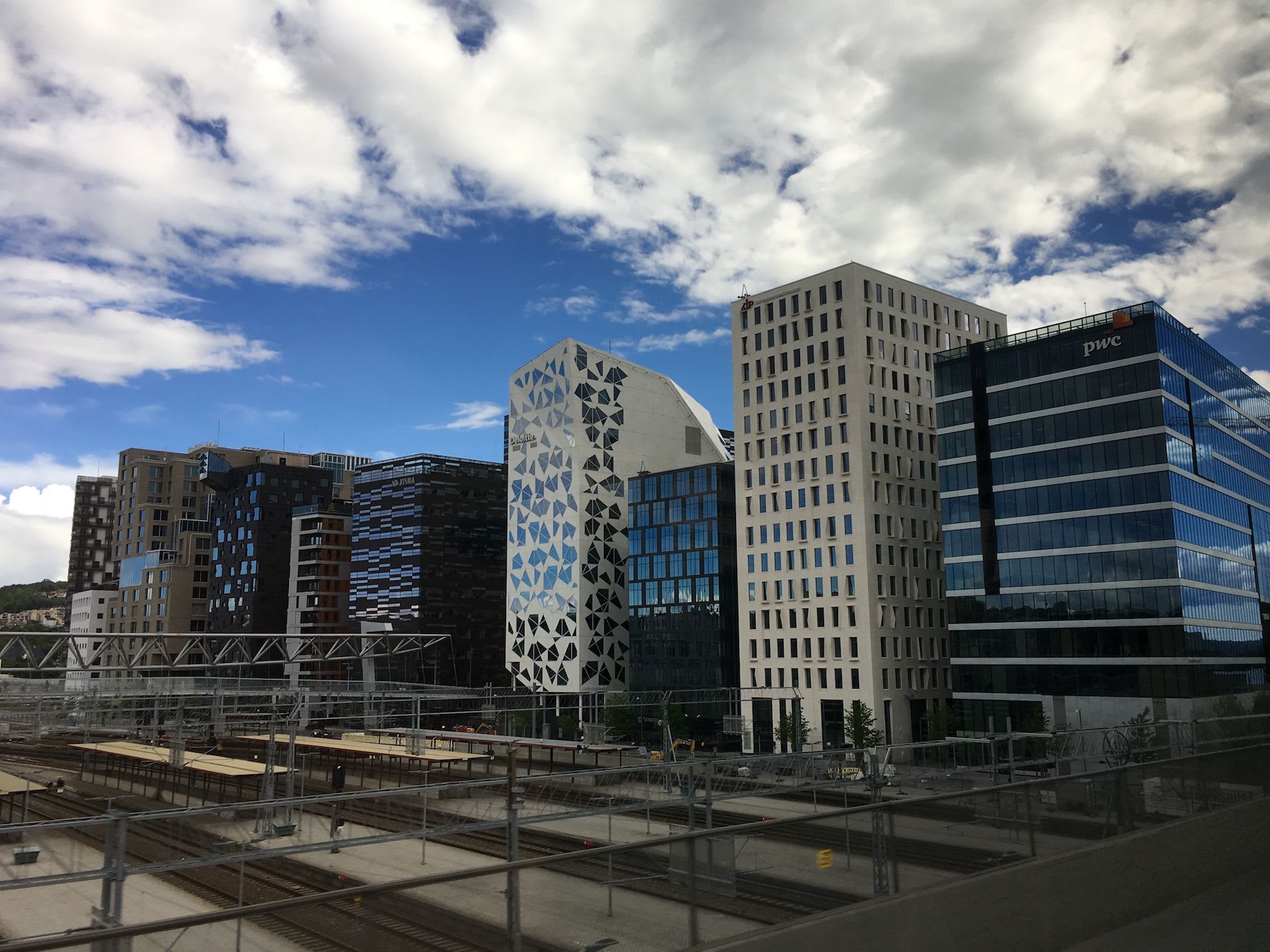 Barcode-Viertel in Oslo mit Hochhäusern, Gleisen und Bahnsteigen unter leicht bewölktem Himmel.