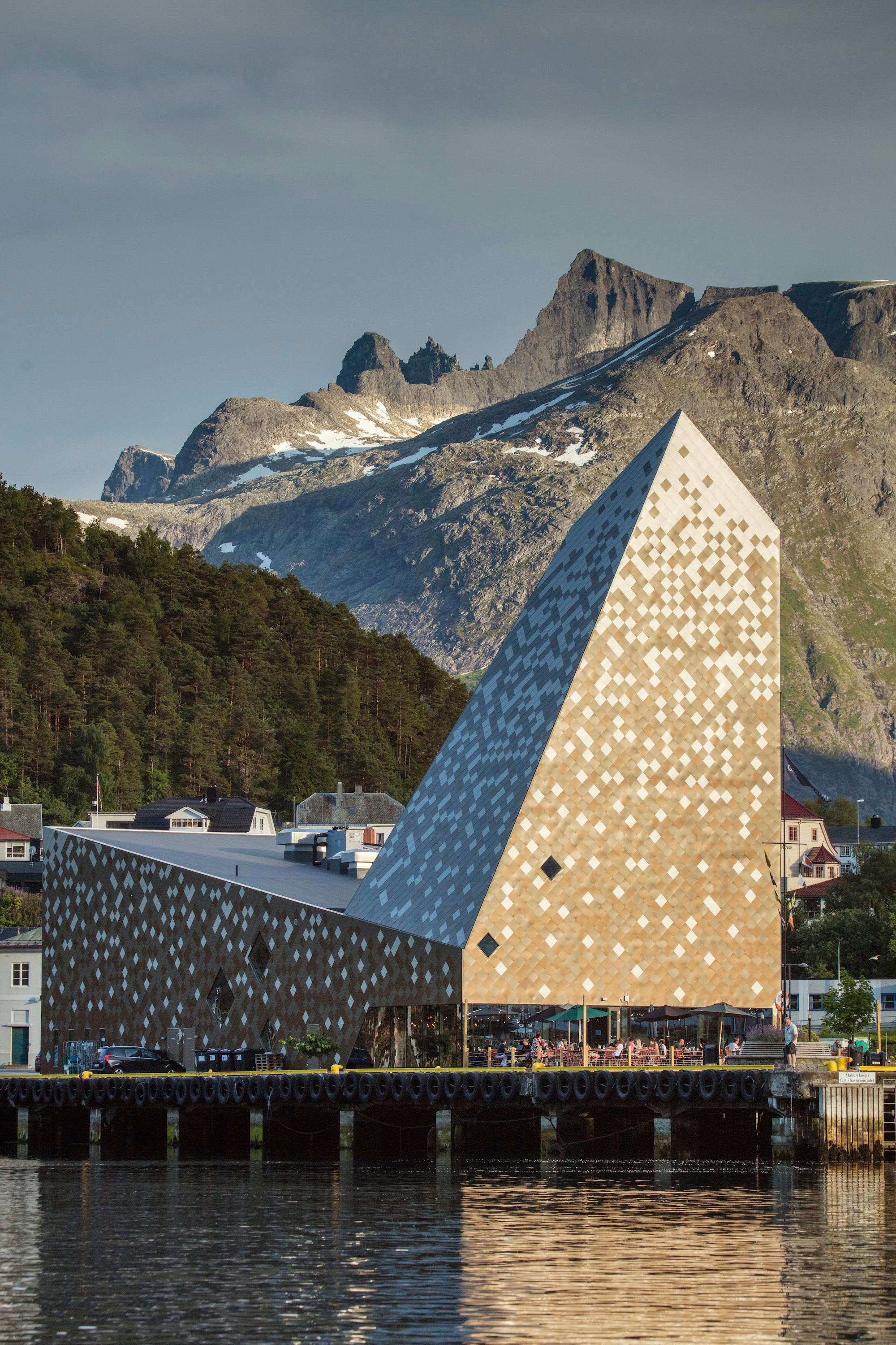 A modern architectural building with a geometric facade of beige and white tiles, located near a dock.