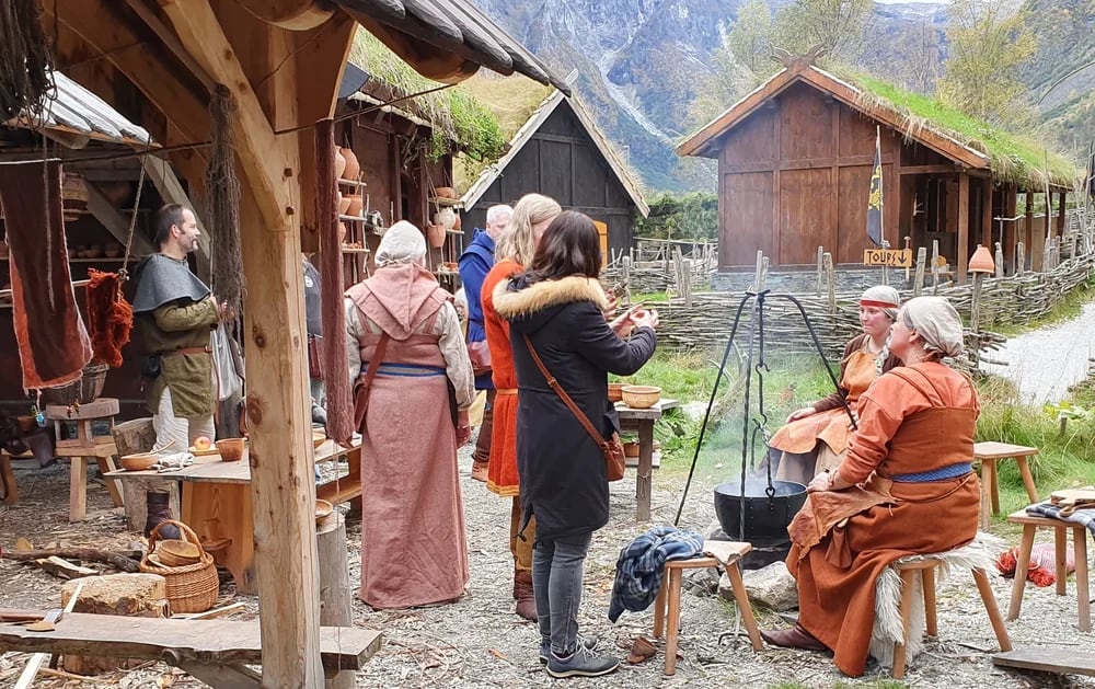 Vikings and tourists gathered around a fire pan in Gudvangen Viking village learning about Viking cooking