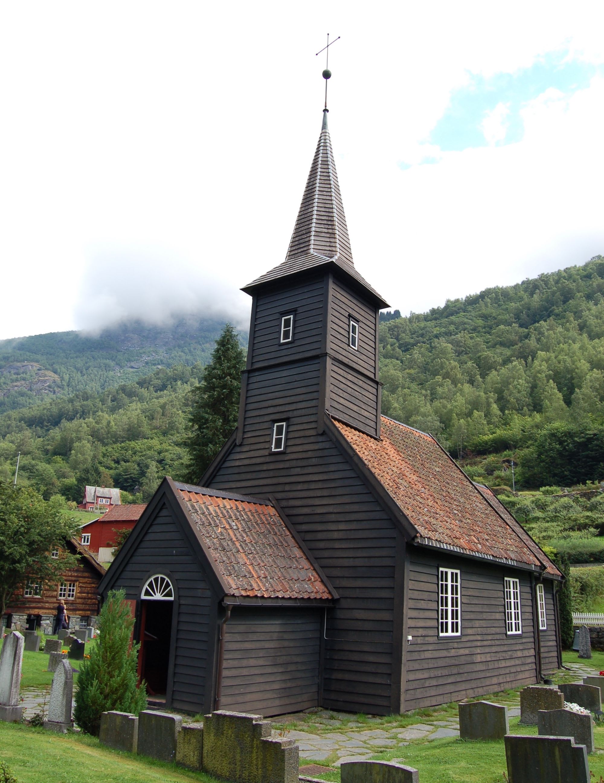 Traditional church with spire, red roof, and cemetery in green mountain valley.