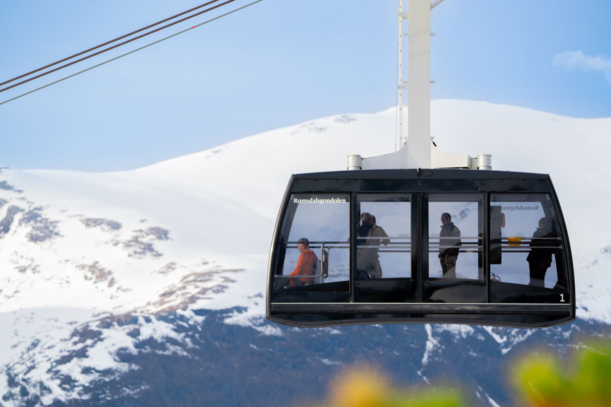 Romsdalsgondolen cable car suspended against a backdrop of snow-covered mountains, with passengers inside.