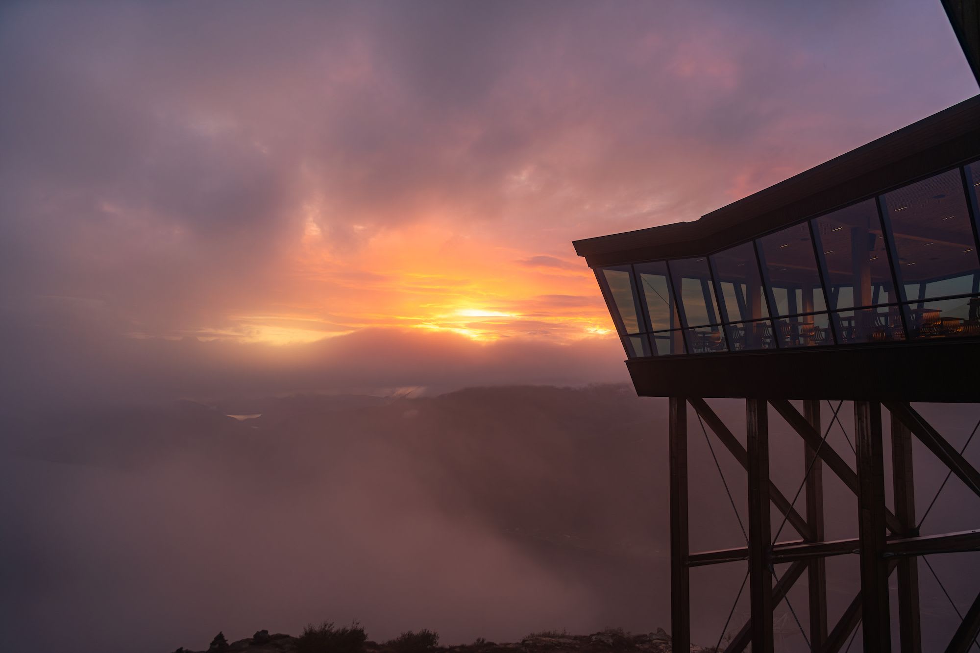 A modern structure with large glass windows, perched on stilts, overlooking a breathtaking sunset.