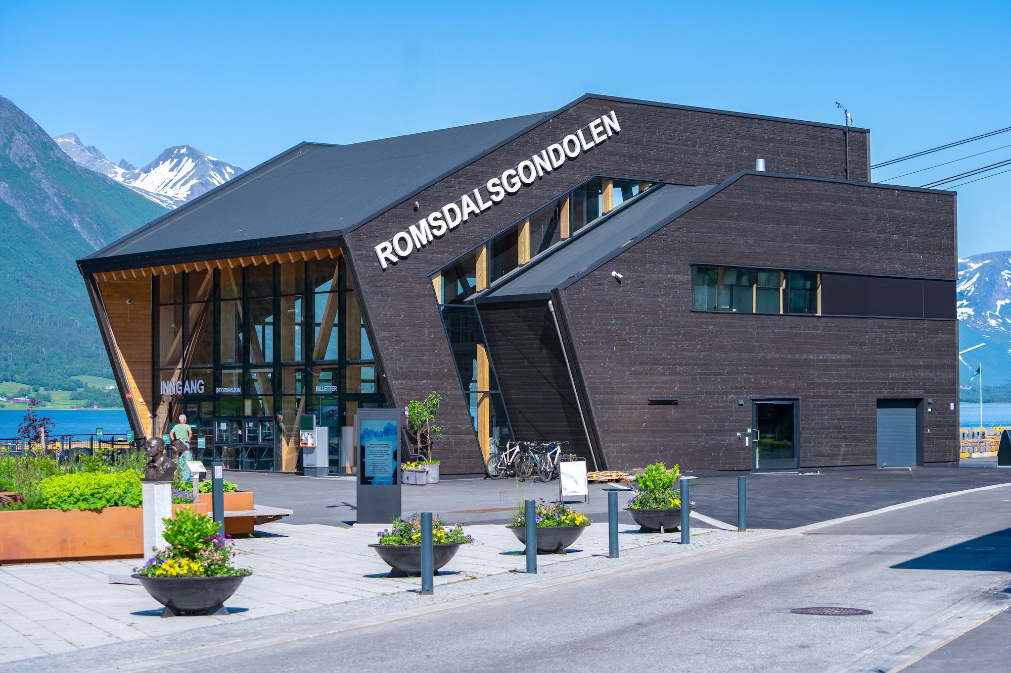 A modern building with the name "Romsdalsgondolen" displayed prominently on the facade, surrounded by snow-capped mountains.
