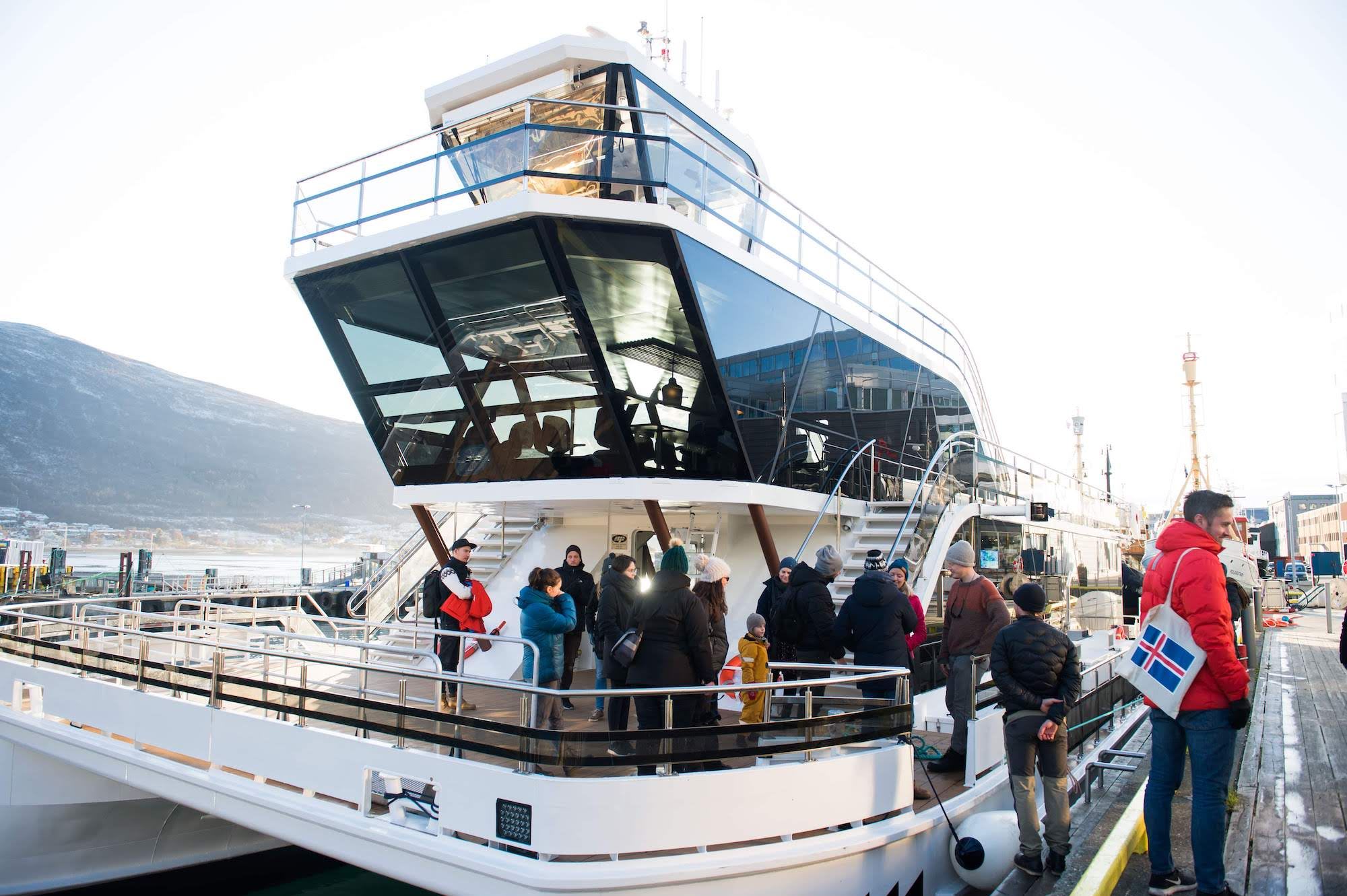 Familier går ombord på moderne båt med fjell i bakgrunnen.
