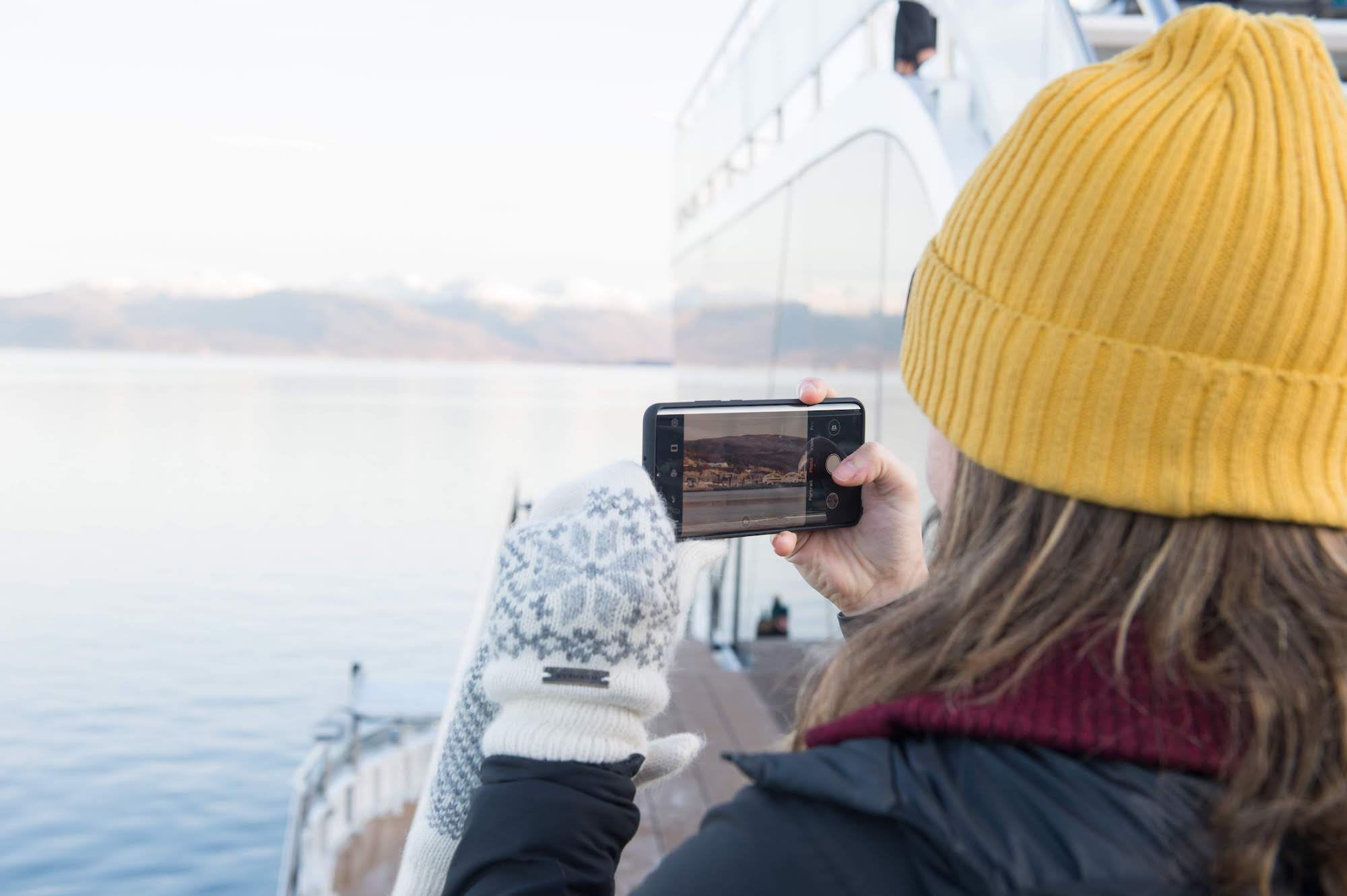 Frau macht Foto auf Boot, Schneegipfel im Hintergrund.