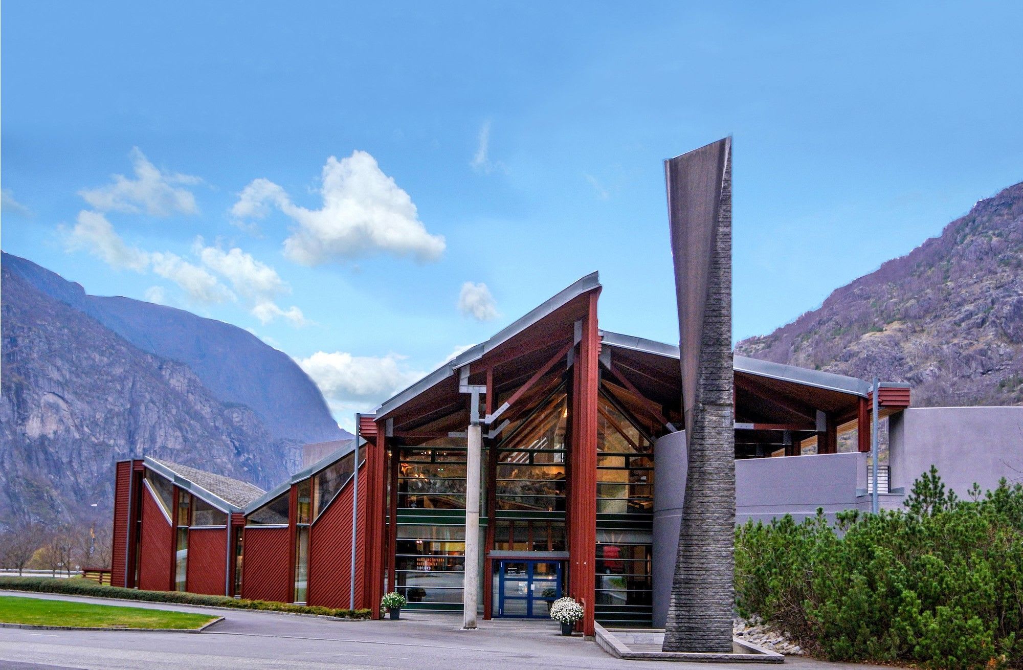 Modern red glass building at the Norwegian nature center Hardanger, situated between mountain cliffs.