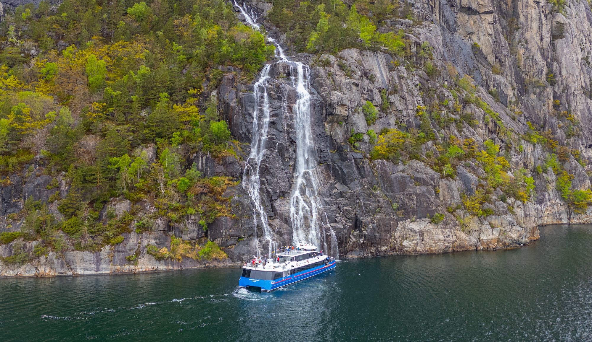 Electric cruise boat sails close to waterfall in Lysefjord