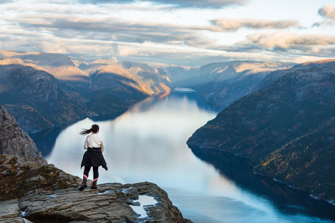 Person i friluftsutstyr på Preikestolen, med utsikt over Lysefjorden, himmelrefleksjoner