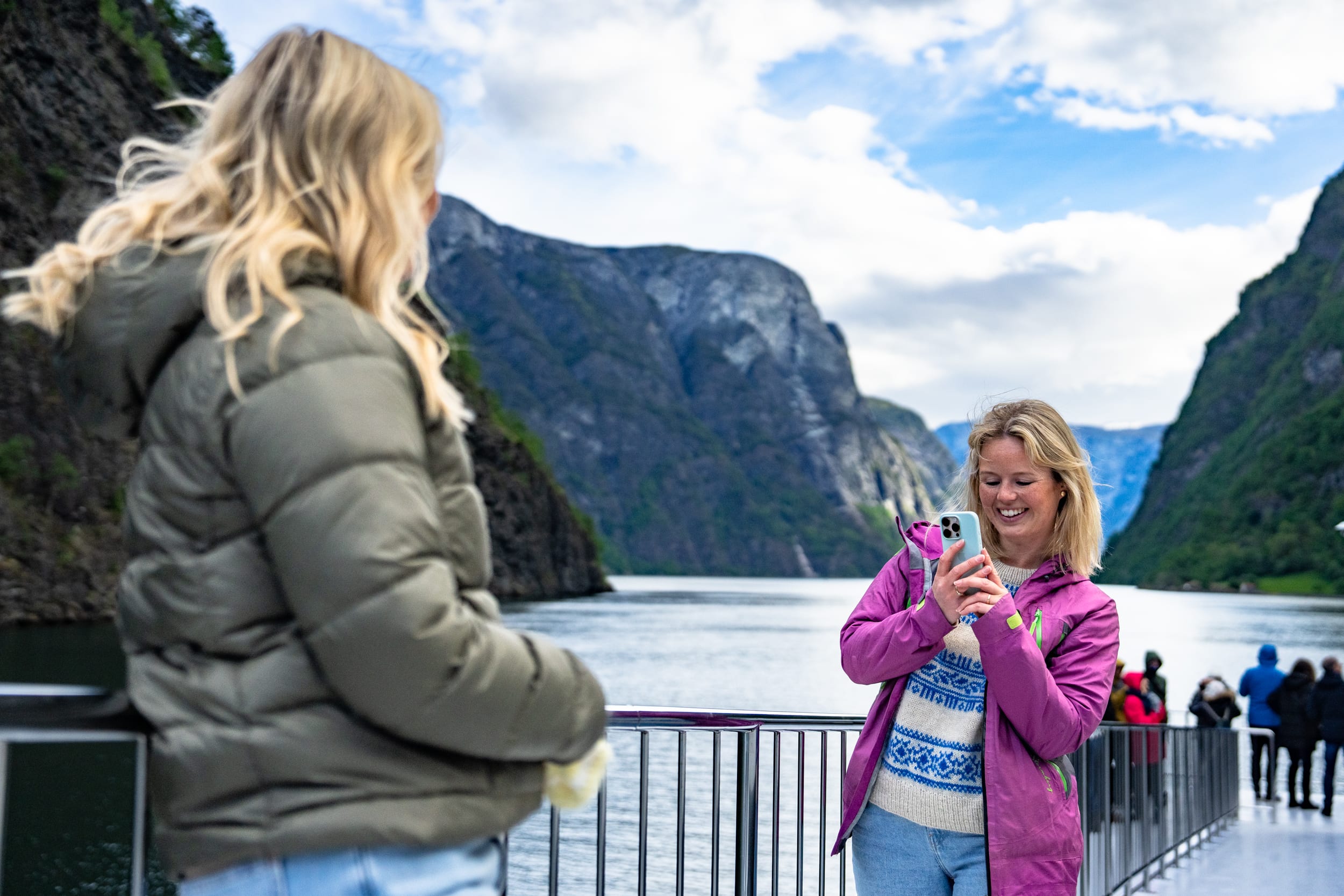Two women enjoying deck views on fjord cruise between Flåm and Gudvangen through UNESCO-listed Nærøyfjorden landscape