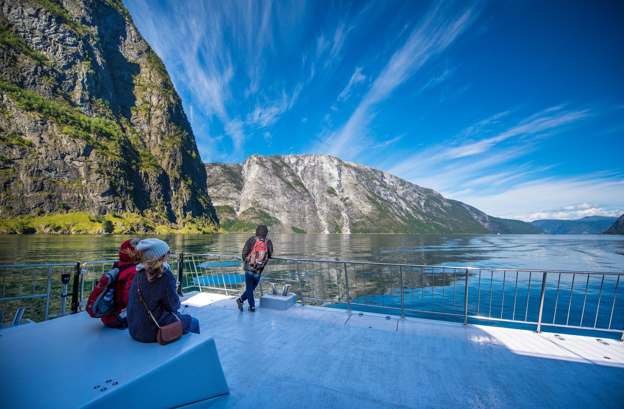 Passasjerer på båtdekket nyter utsikten over Nærøyfjorden, omgitt av mektige fjell.