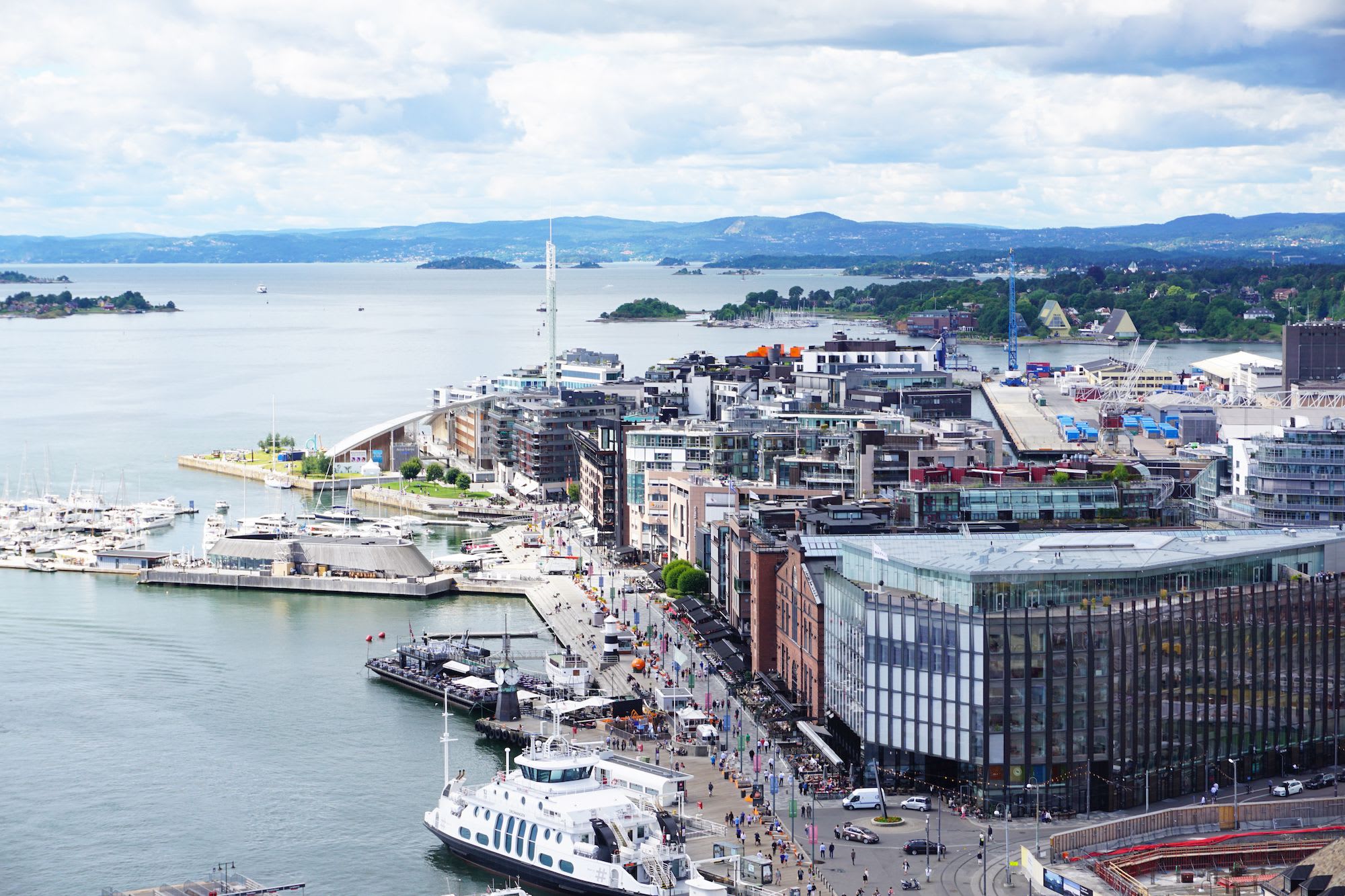A vibrant Oslo along the waterfront with modern architecture, yachts, and people walking along the promenade.
