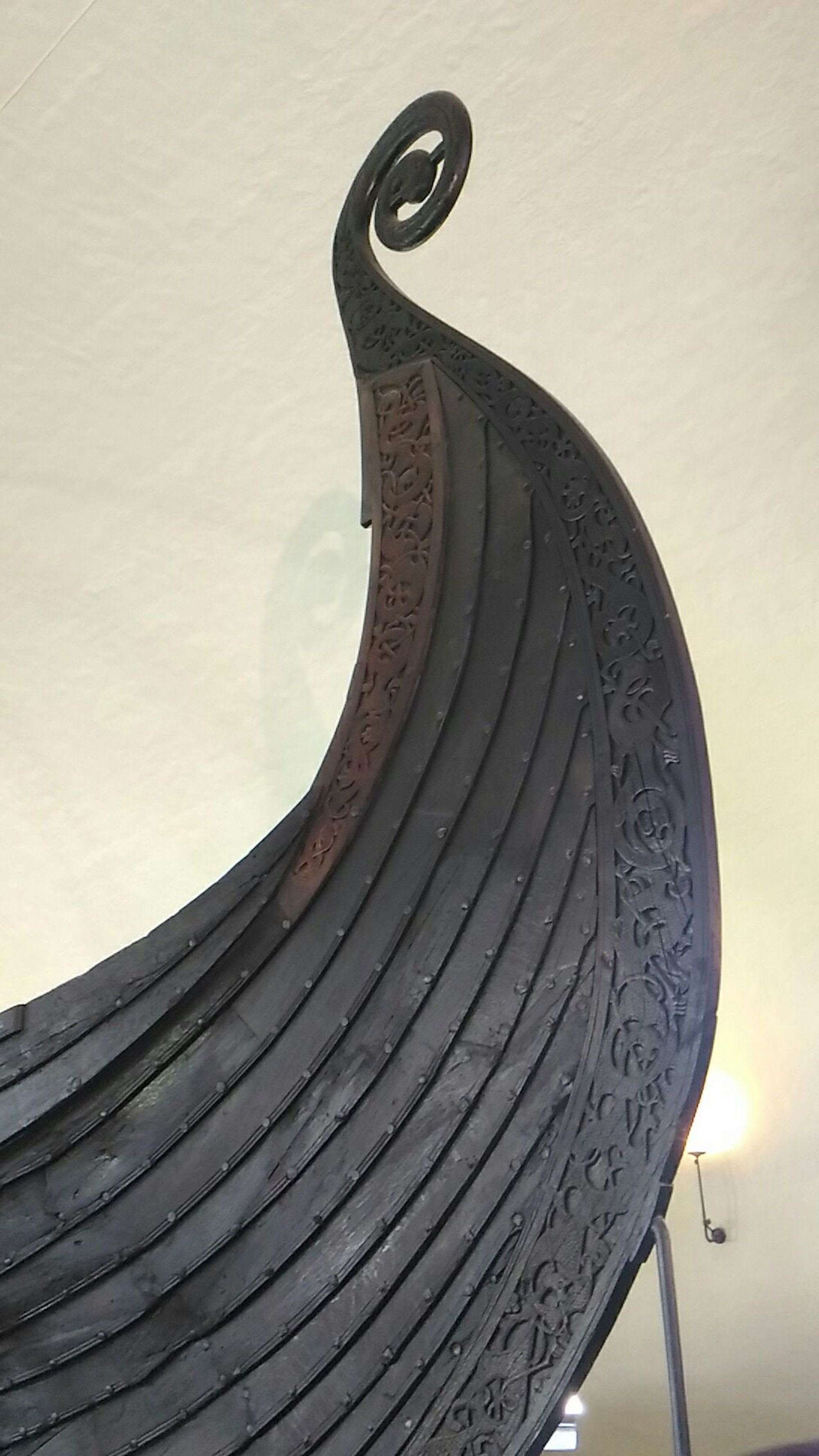 Nærbilde av utskåret vikingskipsbaug med detaljer og spiralform.