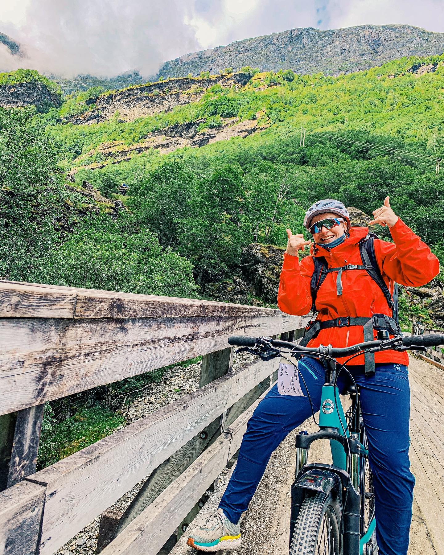 Radfahrer posiert auf Brücke vor grünen Bergen.