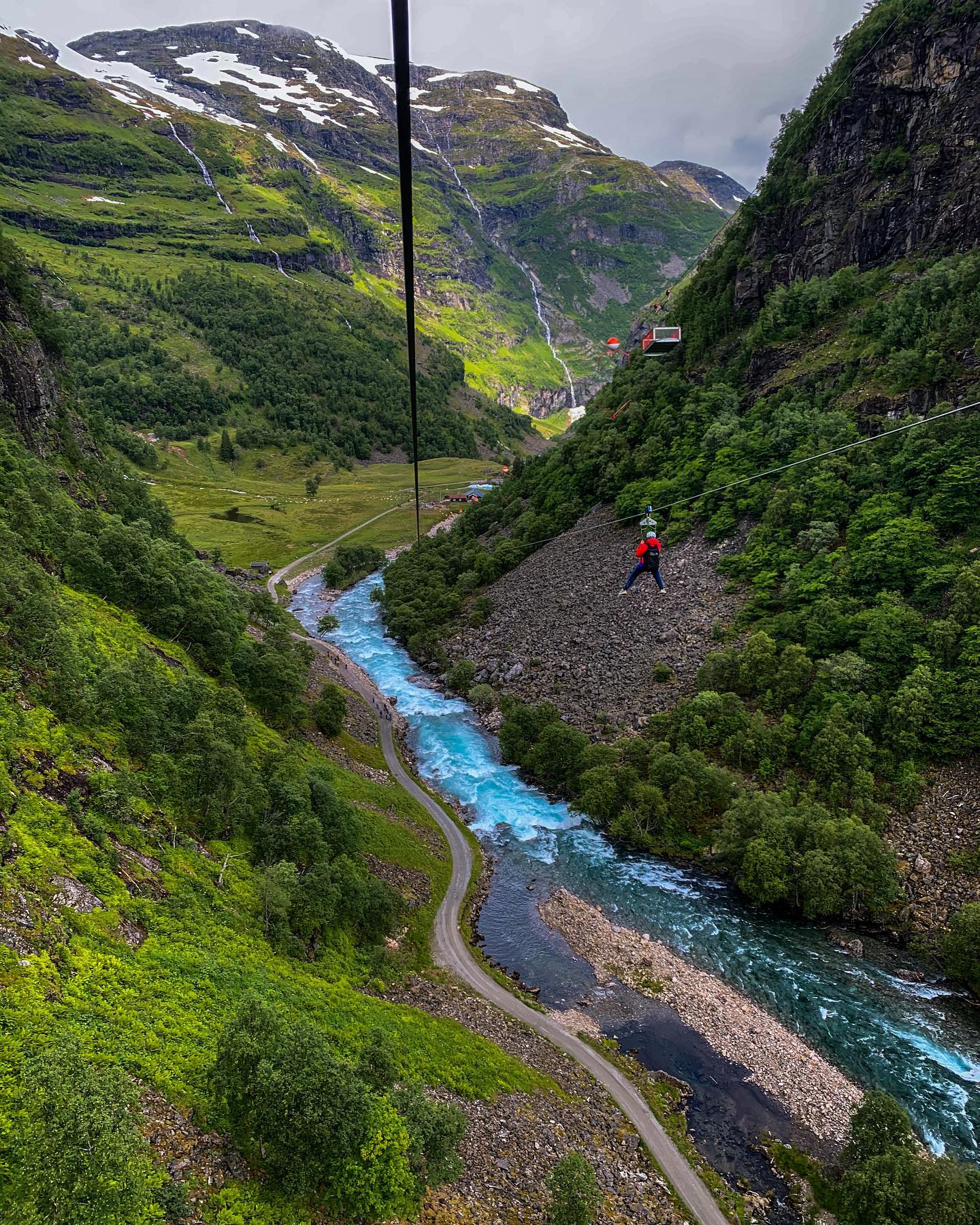 Zipliner mit roter Jacke über blauem Flusstal.