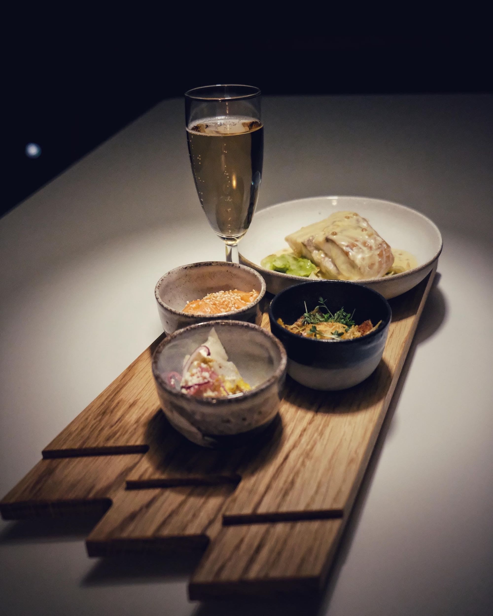 Board with wine and small bowls on white table.