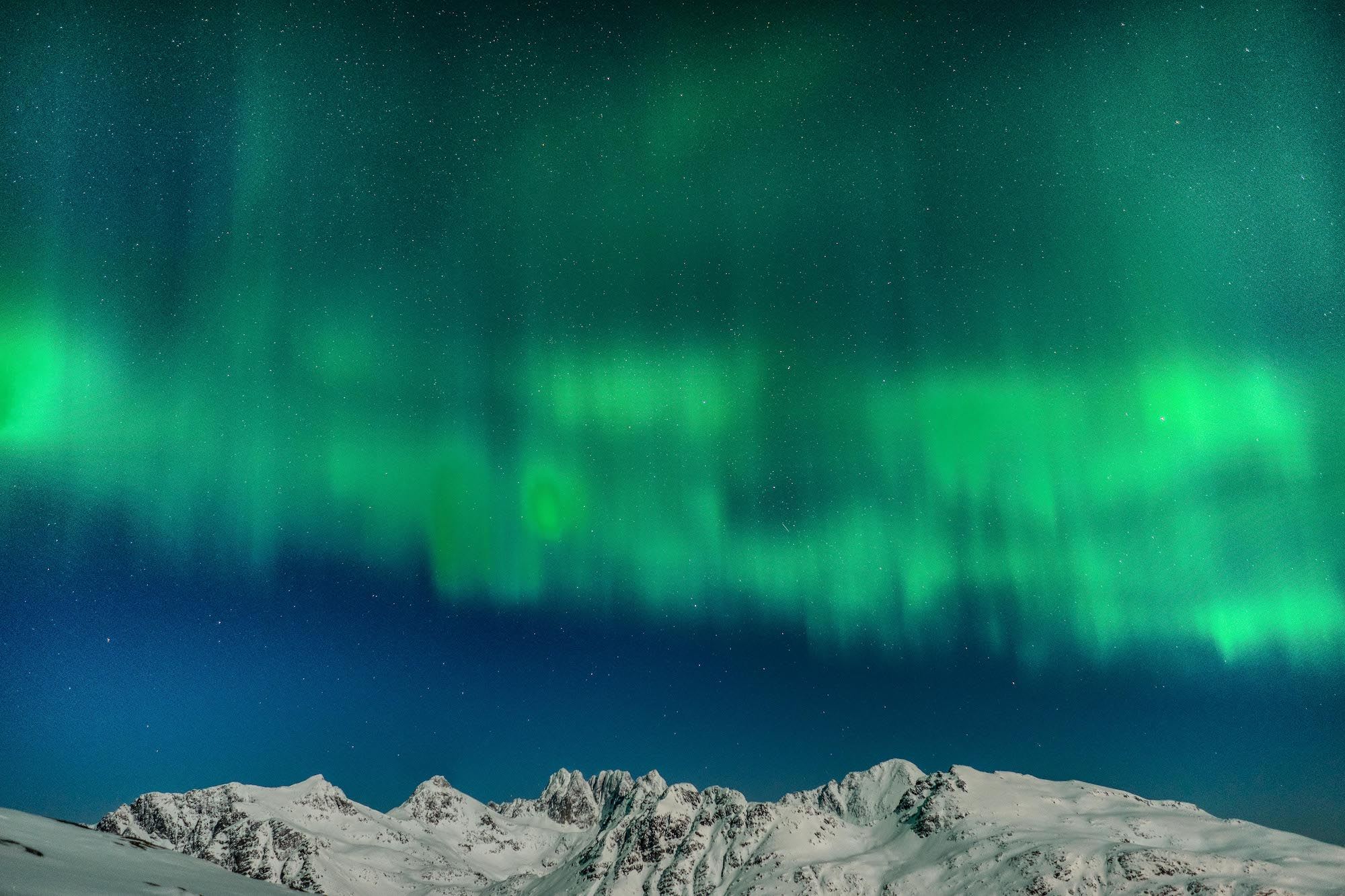 Grønt nordlys over snødekte fjell og stjernehimmel.