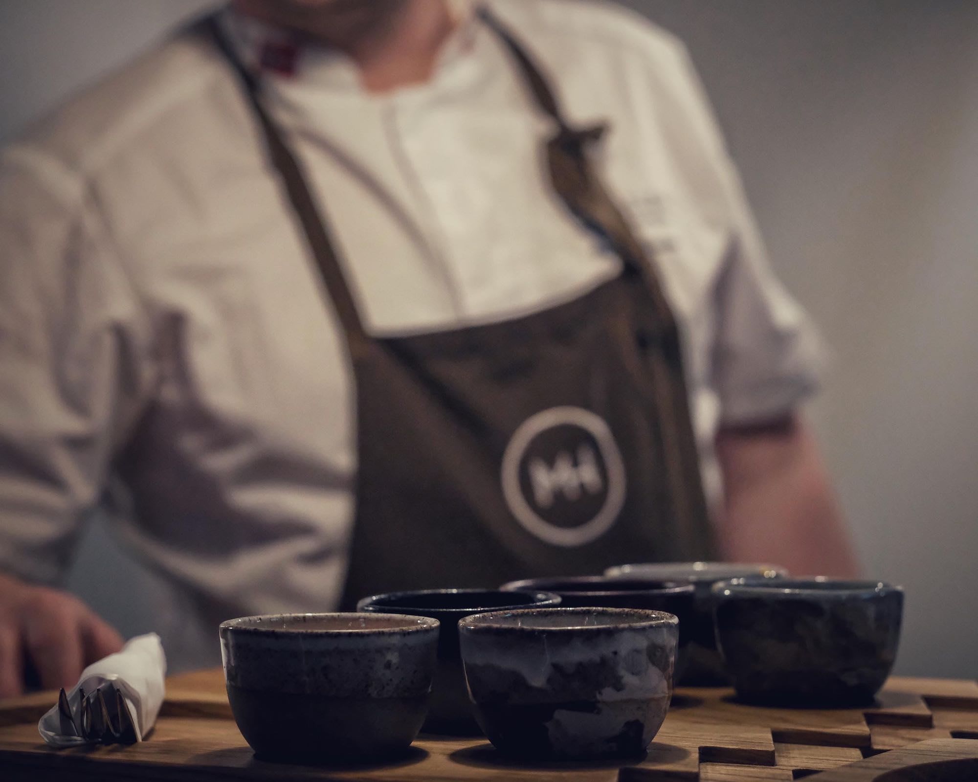 Kokk bak brett med keramikkboller og bestikk.