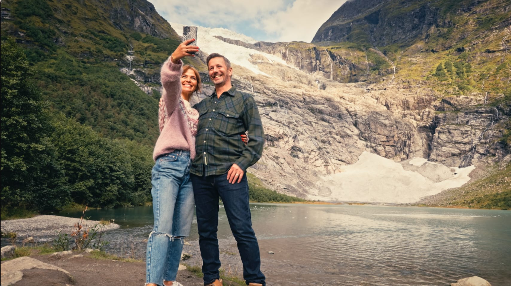 Par som tar bilde ved en isbre i Fjærland, omgitt av fjell og brevann på Vestlandet.