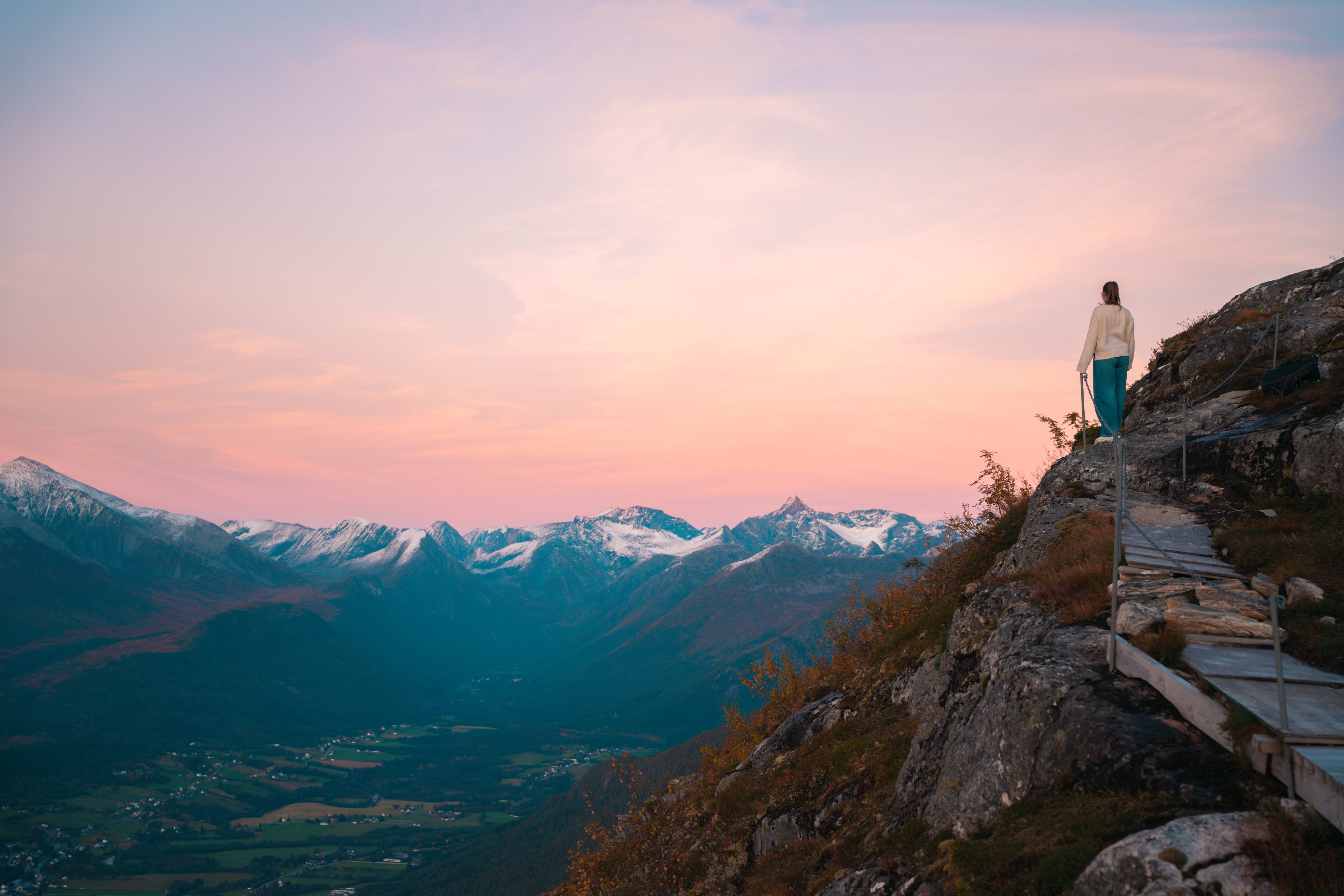 Girl watching sunset at Nesaksla viewpoint in Åndalsnes with snow-covered mountain peaks and pink sky