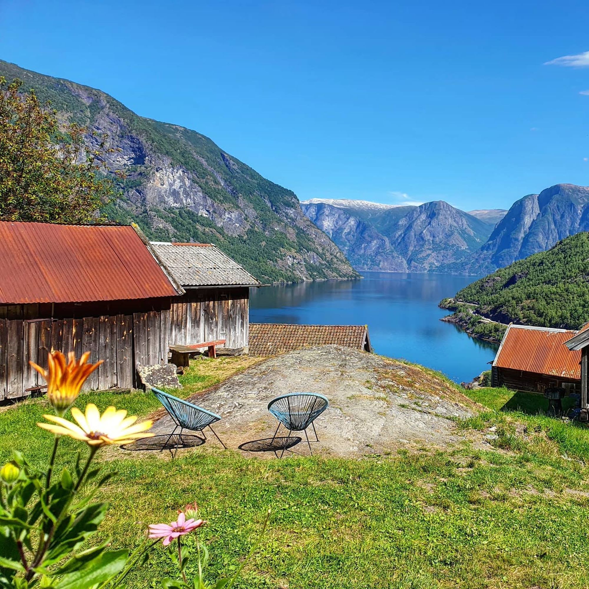 Two chairs on hilltop overlook fjord and cabins.