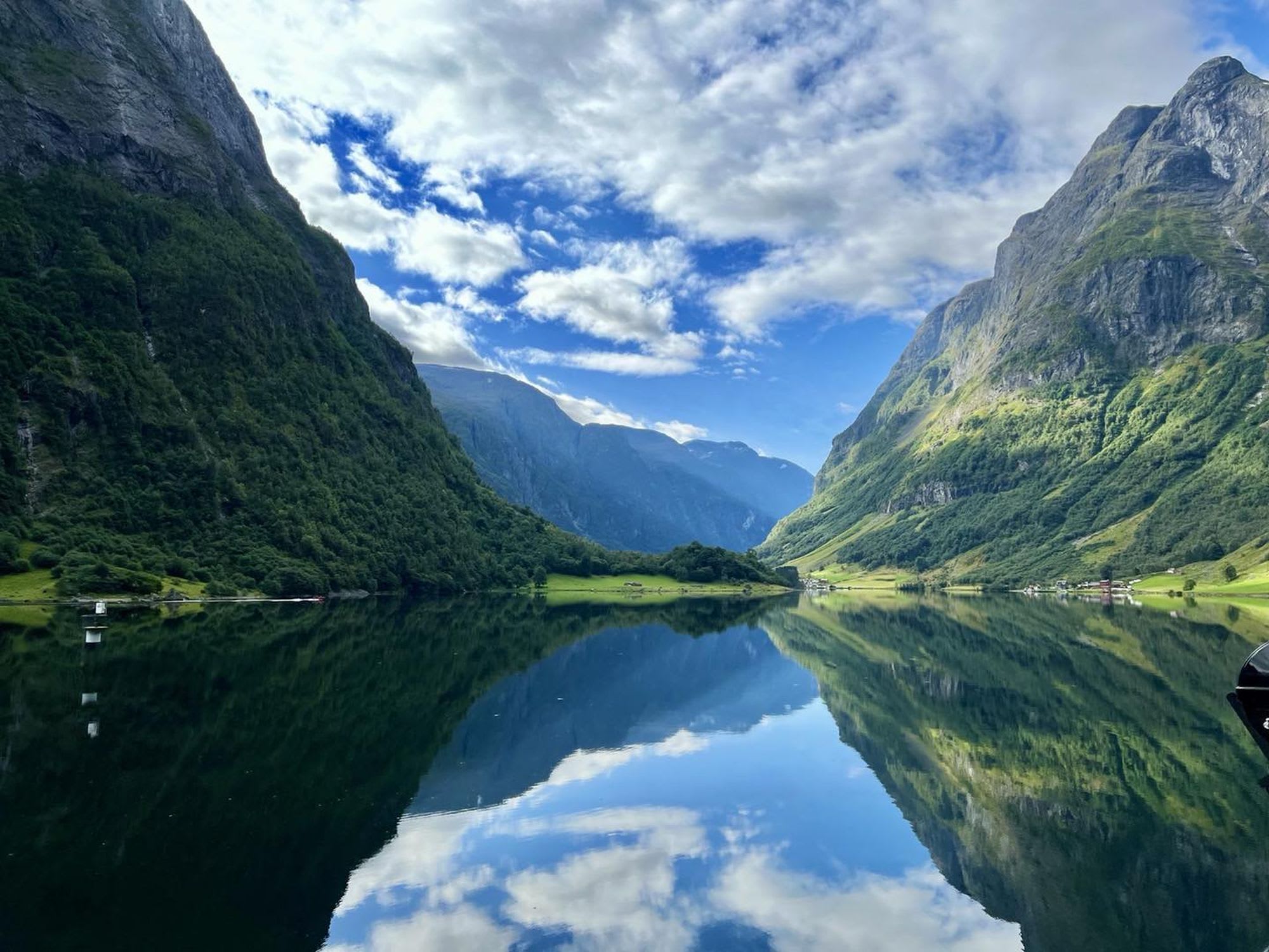 Calm fjord reflects green mountains and cloudy sky.