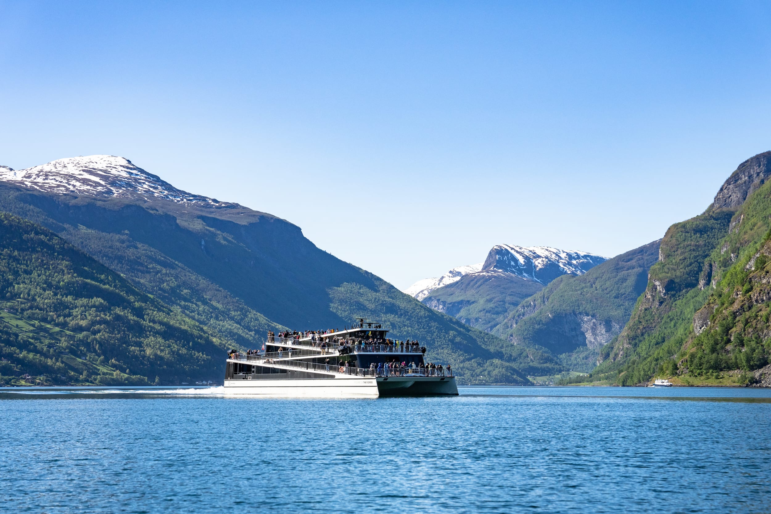 Electric cruise ship sailing through scenic Norwegian fjord with snow-capped mountains