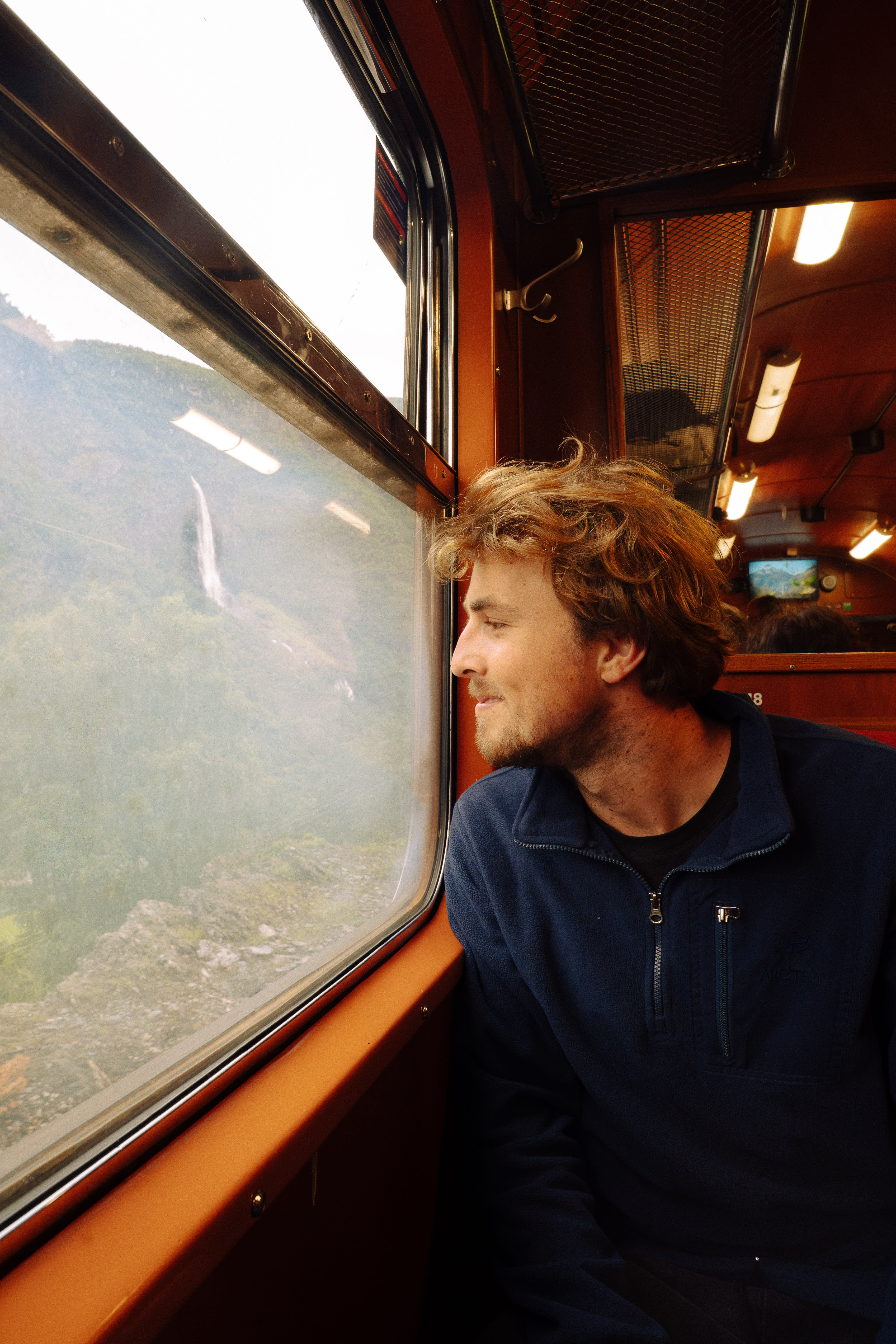 Man looking out of the window on the Flåm Railway, with a waterfall in the background
