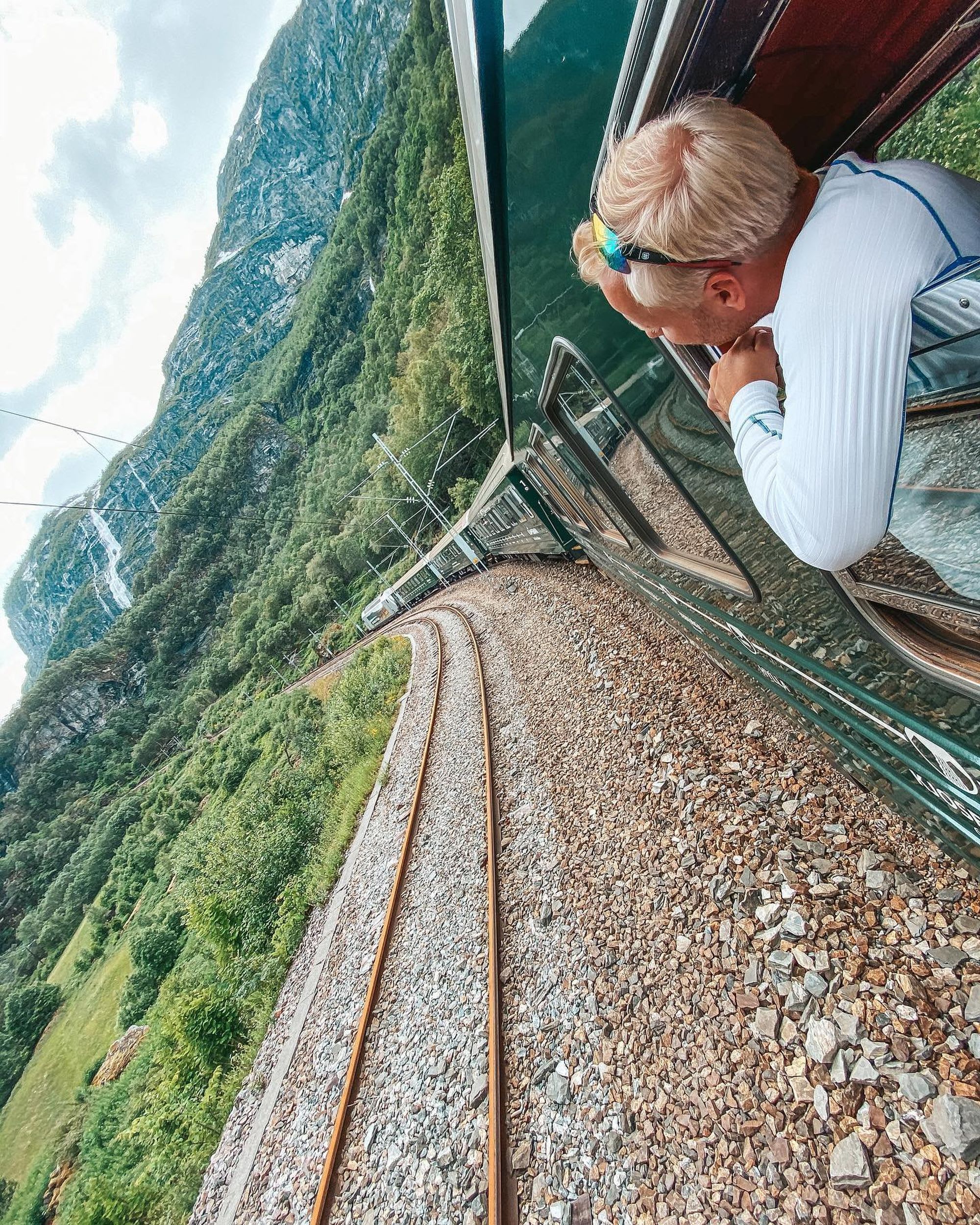Mann nyter utsikten over vakkert landskap fra vinduet på Flåmsbanen mellom Myrdal og Flåm